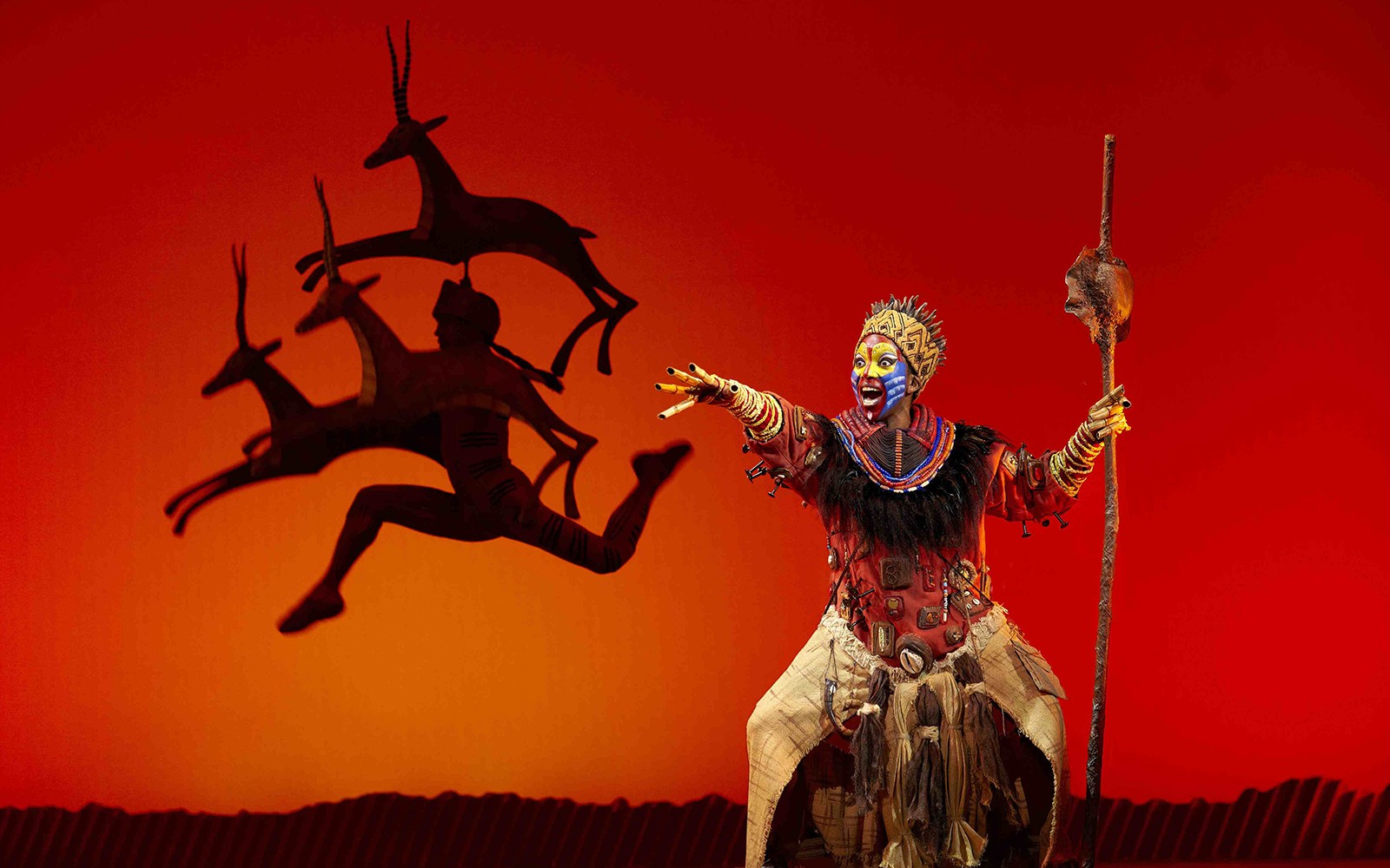 Performer in vibrant costume on stage during The Lion King show in Madrid.