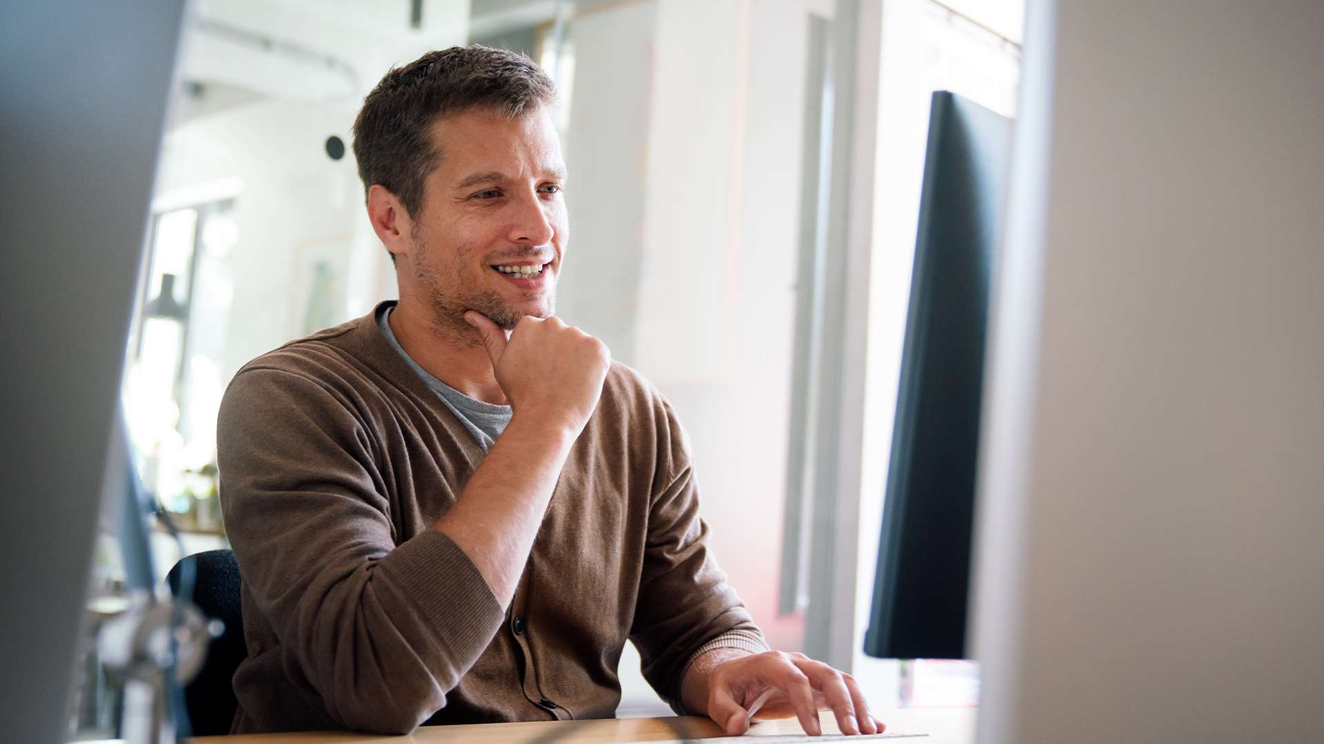 A man working at a computer, smiling and focused. Office workspace.