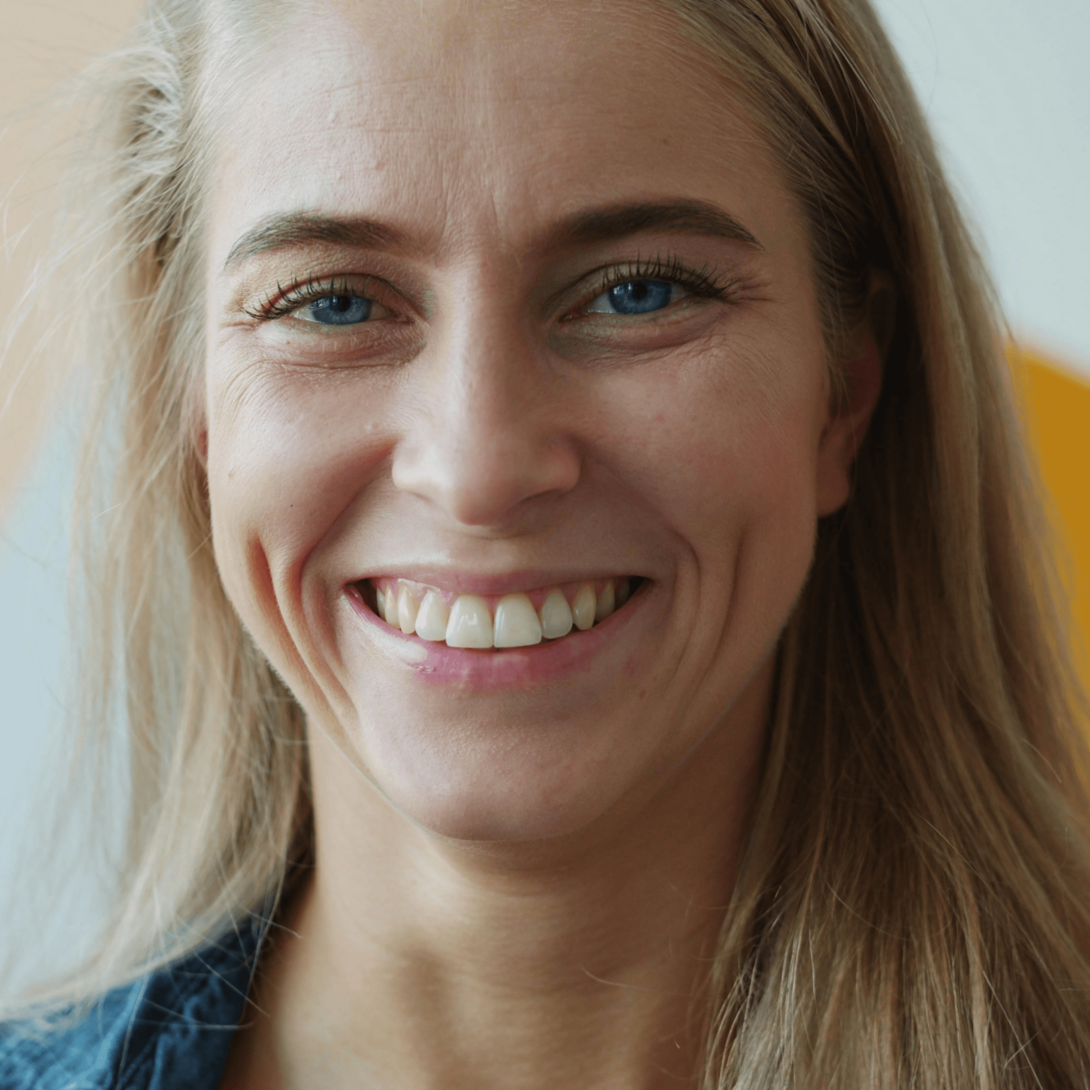 A smiling woman with blonde hair in a denim jacket.