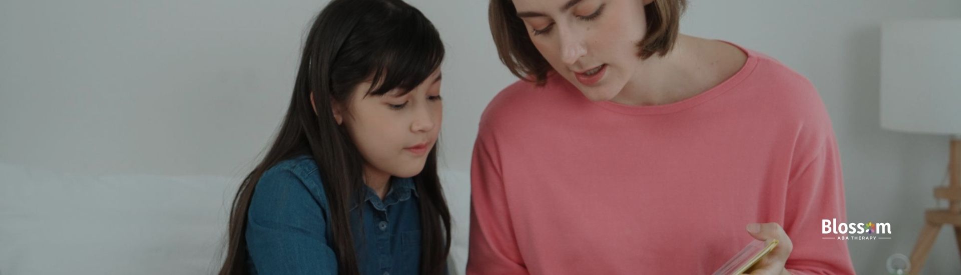  An ABA therapist and a girl reading a book together.