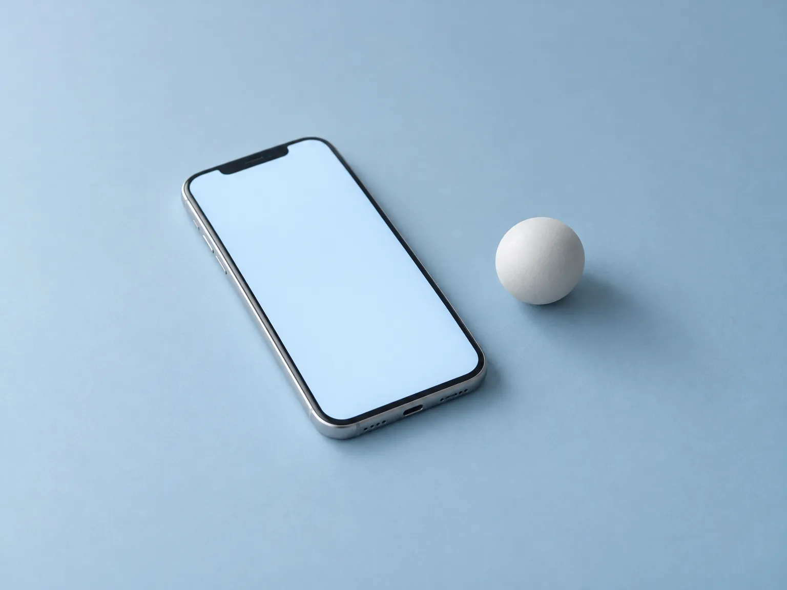 Smartphone with a blank glowing screen beside a small white sphere on powder blue
