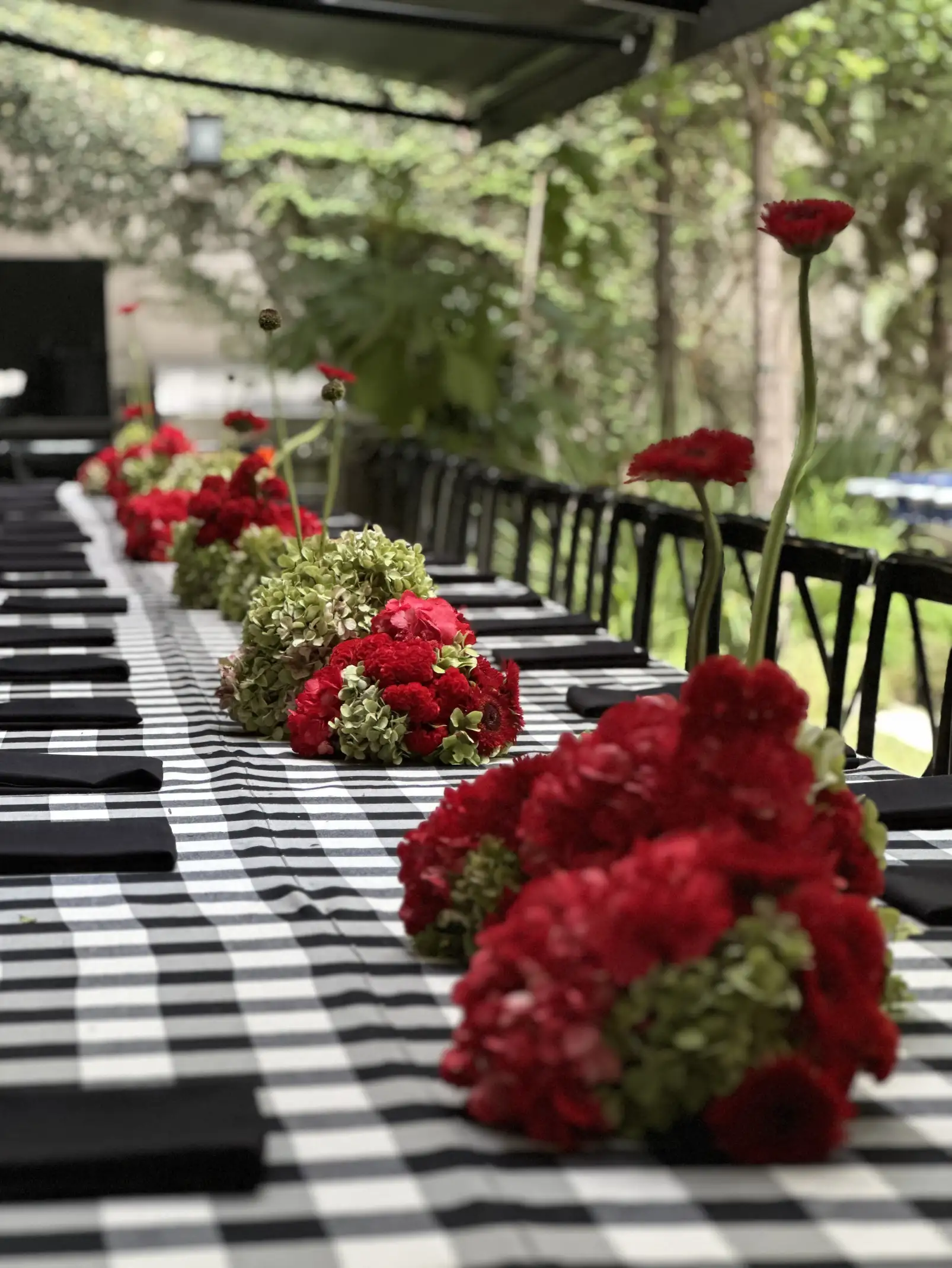 Mesa larga con arreglos florales rojos y verdes sobre mantel blanco y negro para ambientación moderna y vibrante.