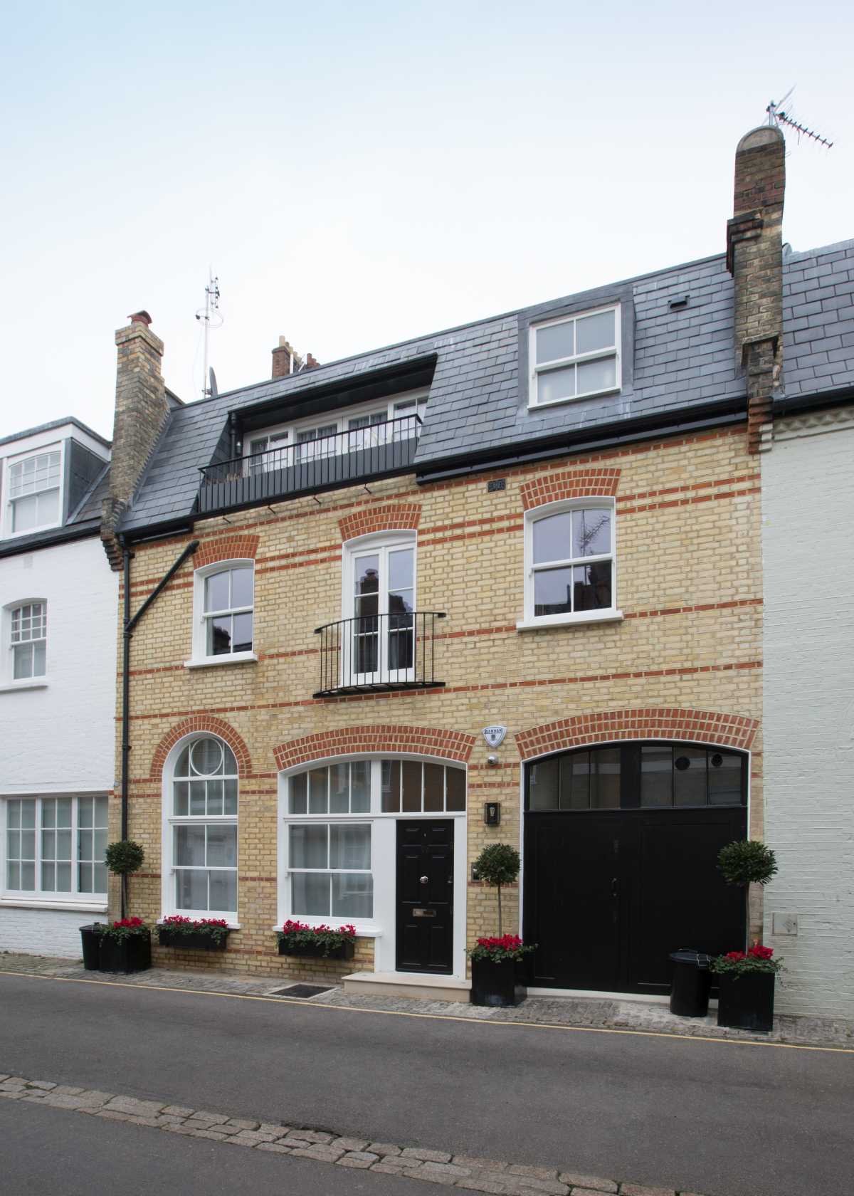 A fully restored historic brick mews house in London, showcasing traditional Flemish bond brickwork restoration, traditional timber sash windows, a Juliet balcony, and sensitive conservation architecture.