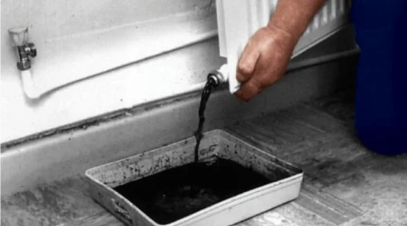 Dark contaminated water being drained from a central heating system filter into a metal tray, showing severe debris build-up