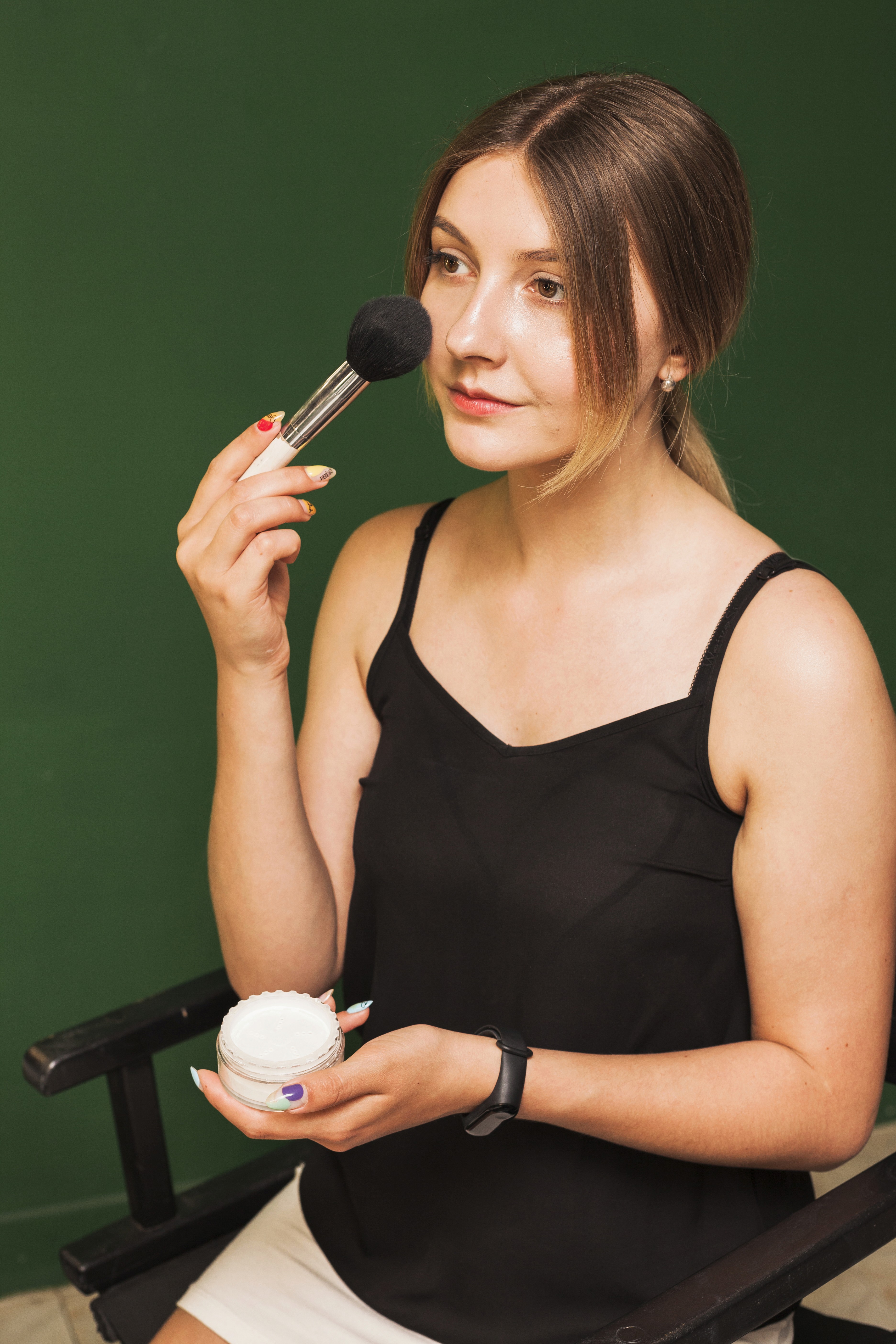 A stylish South Asian woman in her late 20s, with flawless makeup, in a chic salon environment, holding makeup brushes.