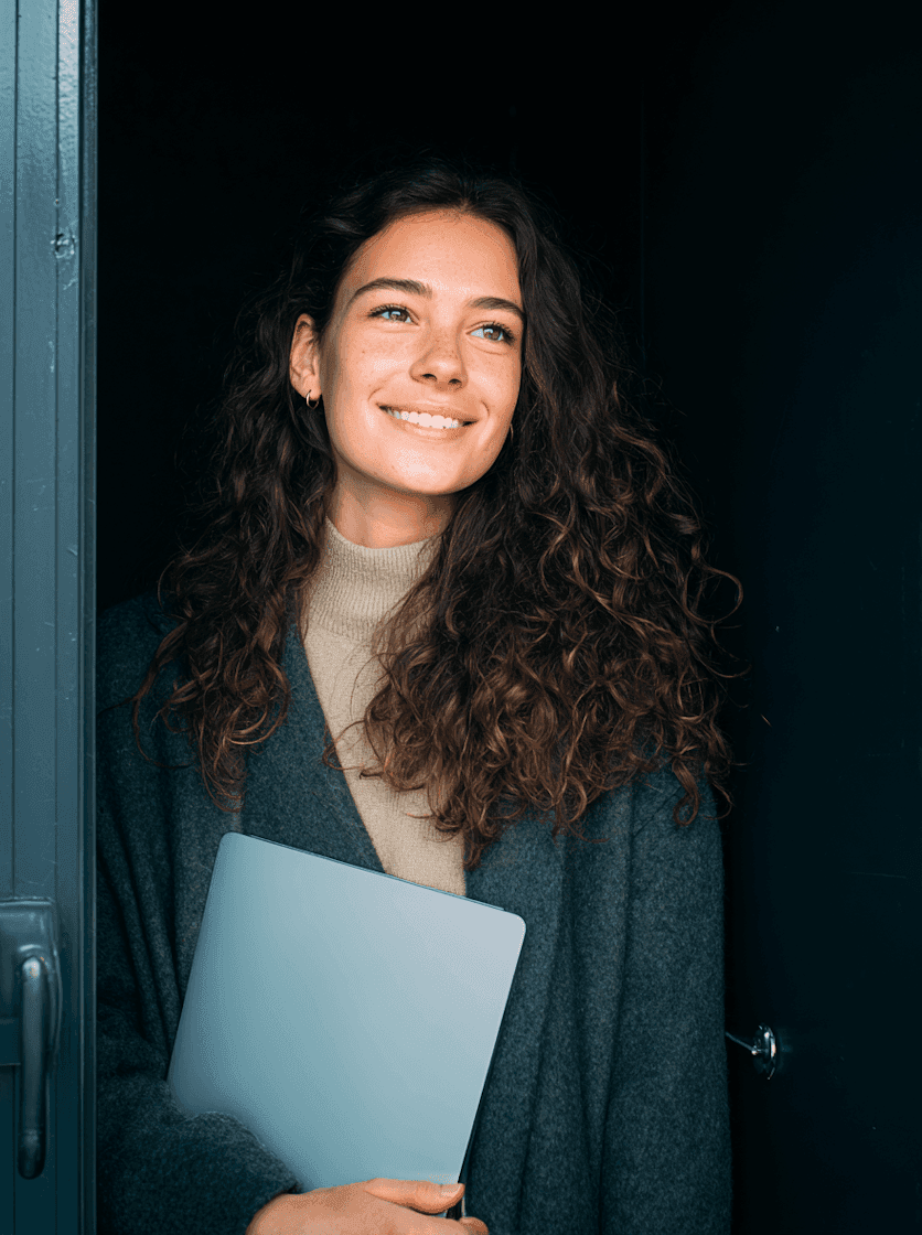 A woman with curly hair is holding a laptop, looking engaged and focused on her work.