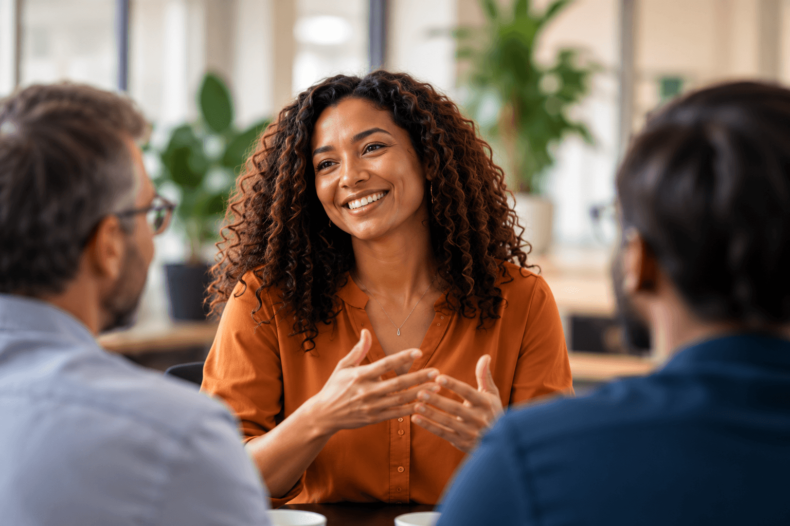 A woman in orange speaking with colleagues in a professional conversation.