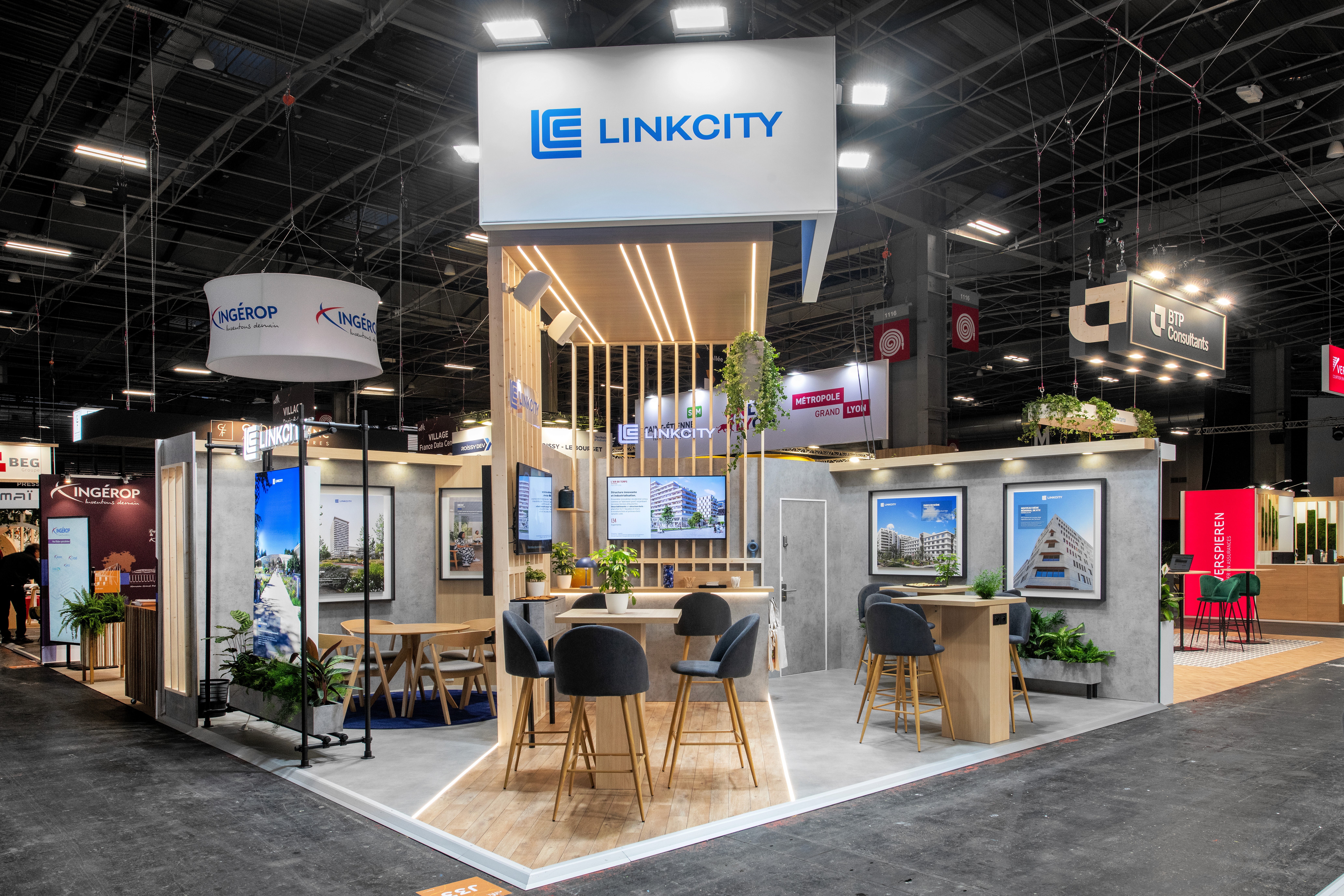 Stand Linkcity Groupe Bouygues salon SIMI 2025 Paris réalisé par Expace – vue frontale avec claustra bois, caisson logo suspendu, visuels projets immobiliers et espace lounge végétalisé