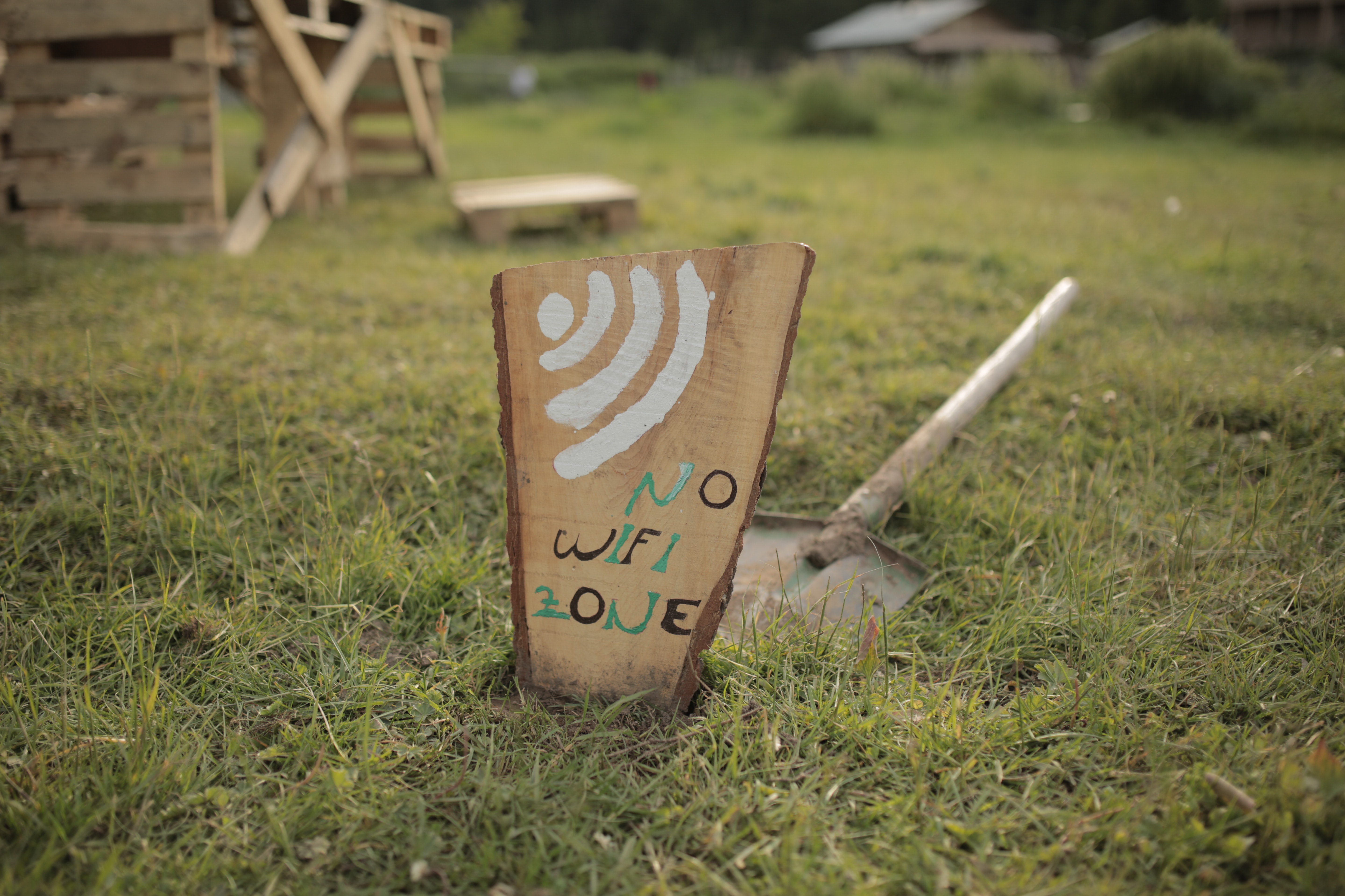 A wooden sign on grass reading ‘No WiFi Here Zone’, symbolizing lack of digital connectivity.