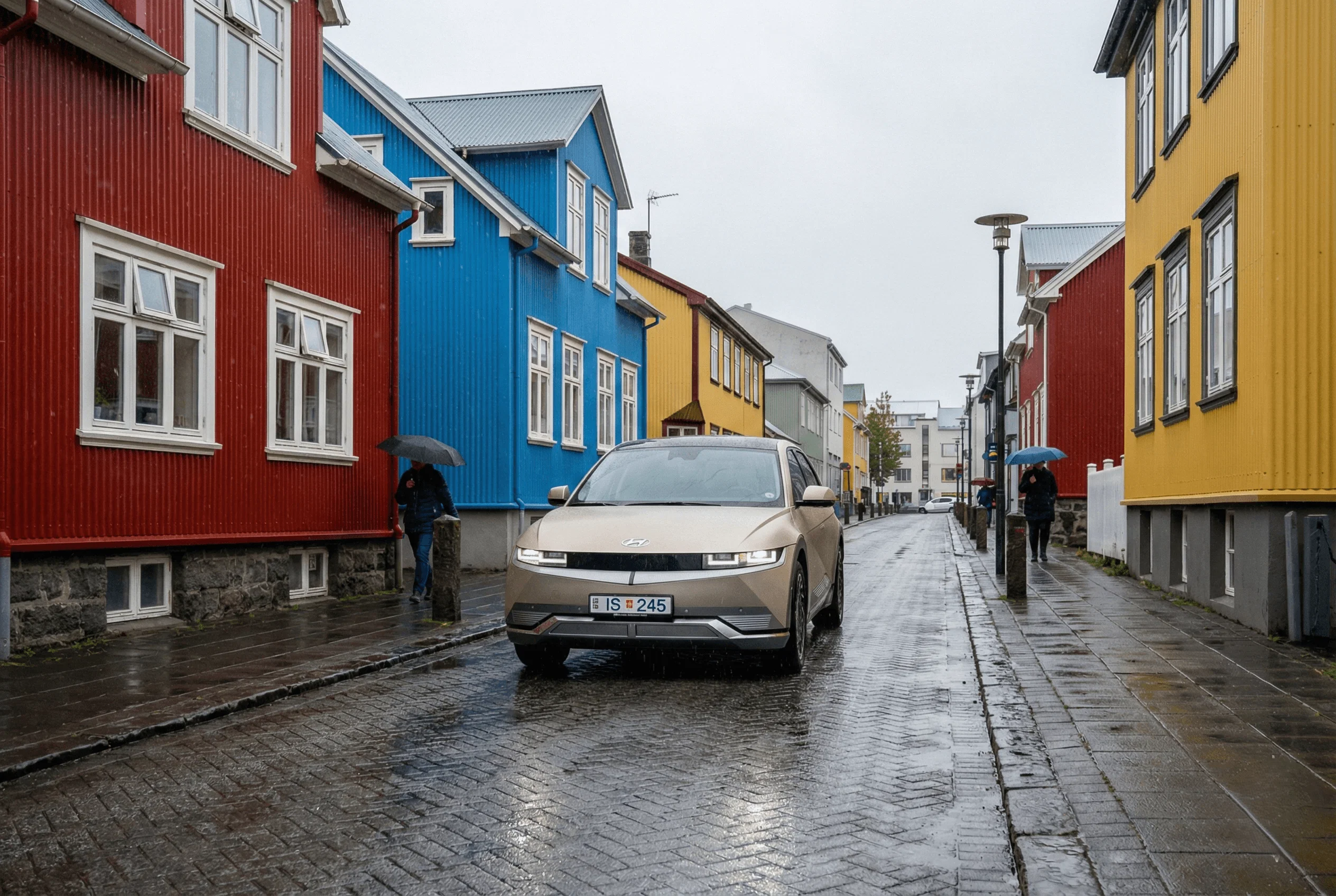 A beige electric SUV driving down a wet street lined with colorful corrugated metal houses in a city.