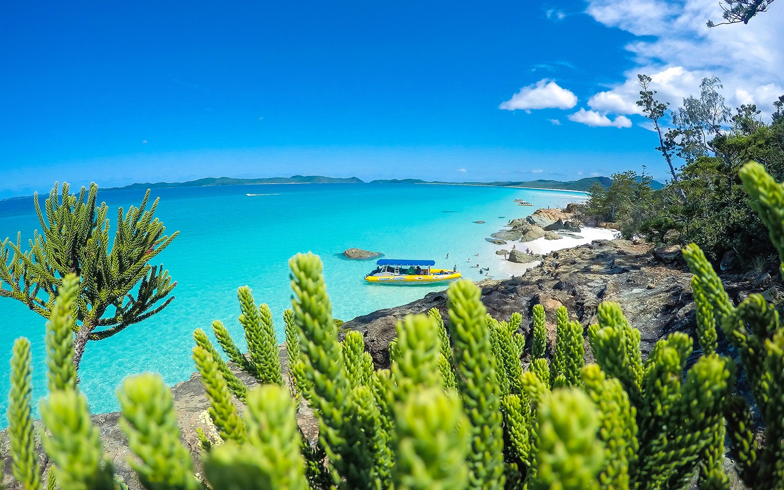 חוף וויטסנדייז עם מים טורקיז ורפסודת צהובה ליד חוף סלעי.