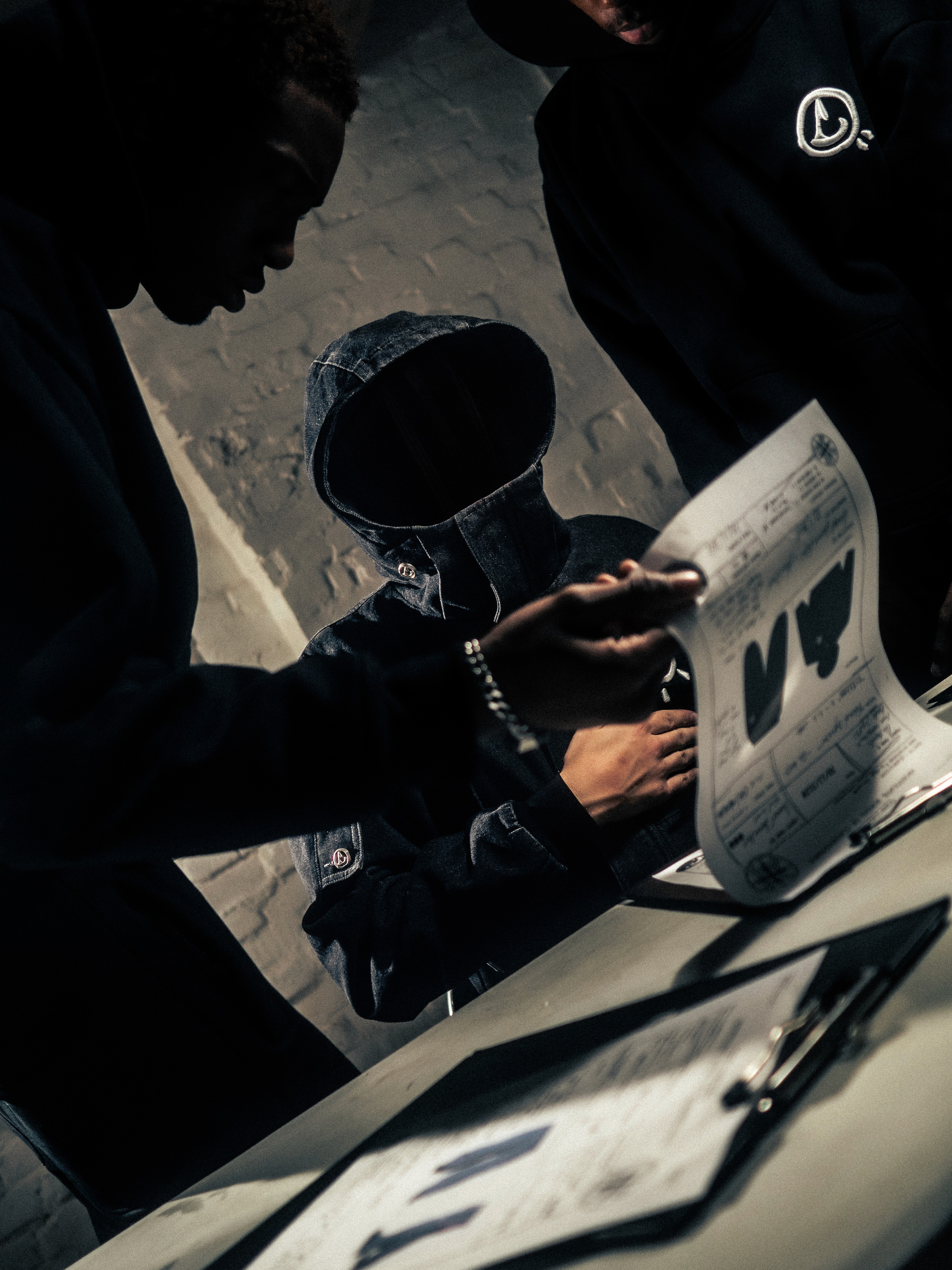 Smiling man in a white hoodie and black pants standing confidently on a bright green football field with empty stadium seats behind.