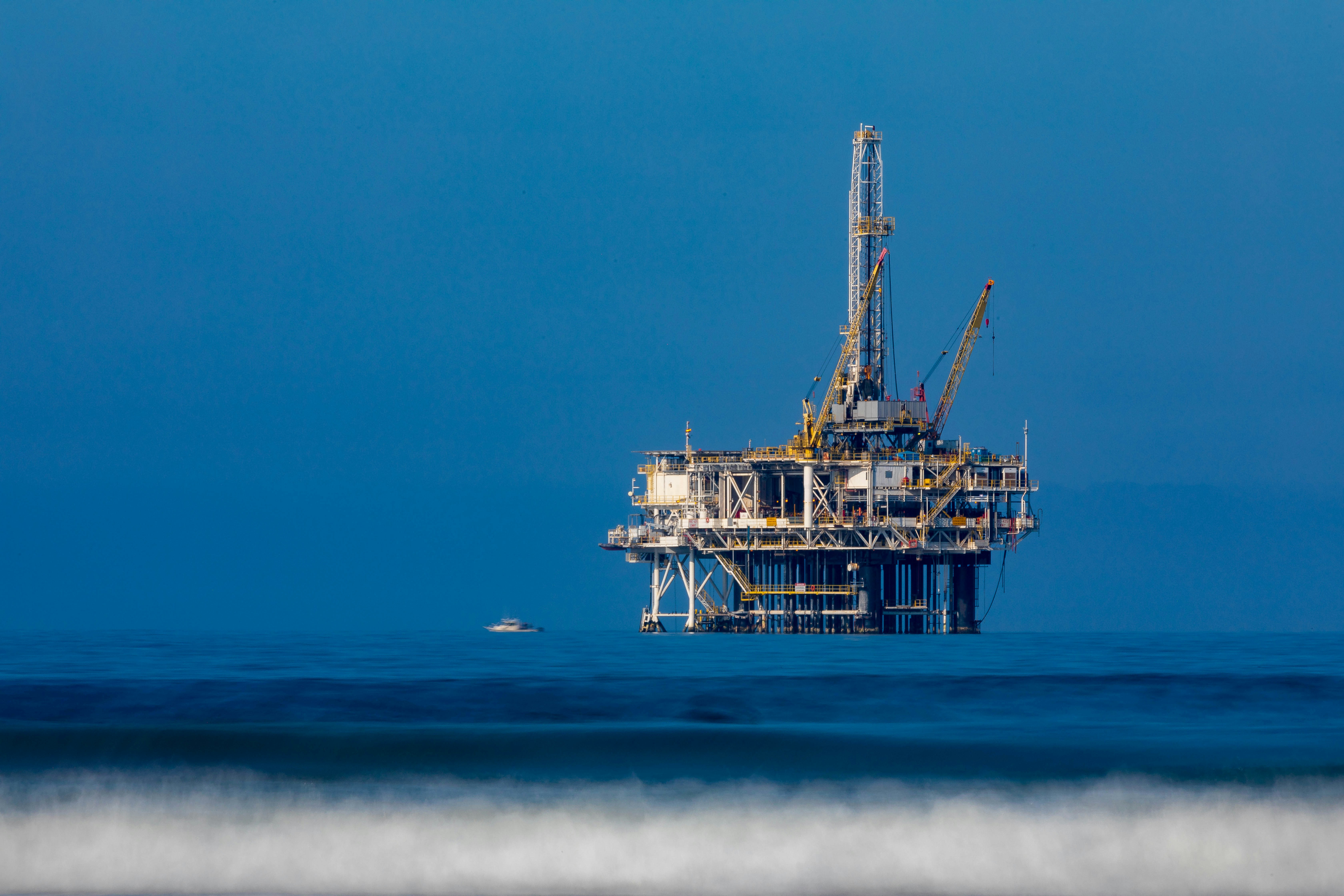 A large offshore oil rig with a prominent crane, situated in the open ocean under a bright sky, by Automech Group