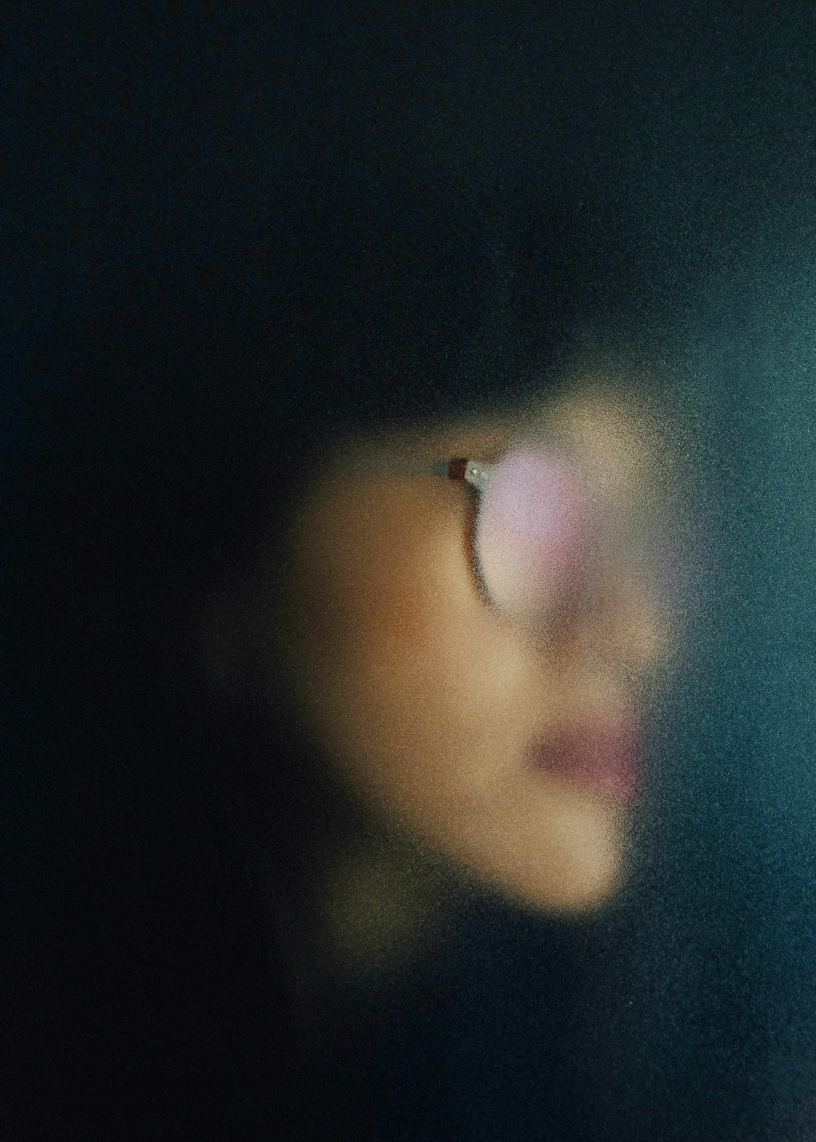 A close-up of a person's profile, with glasses, partially illuminated against a dark background.