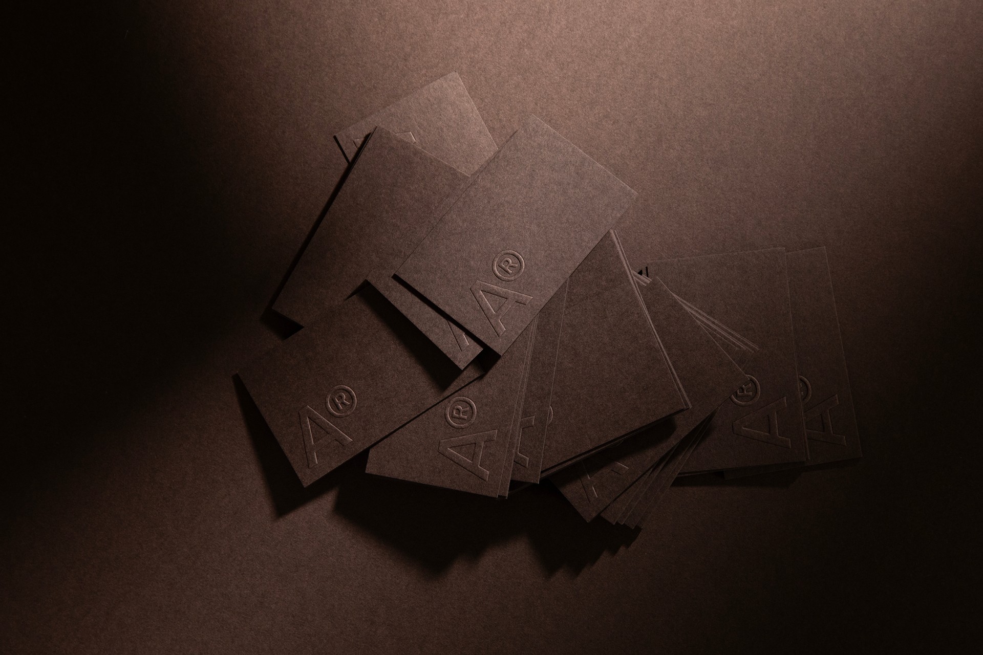 A picture of brown businesscards laying face up on a brown background, showing the AR-logo.