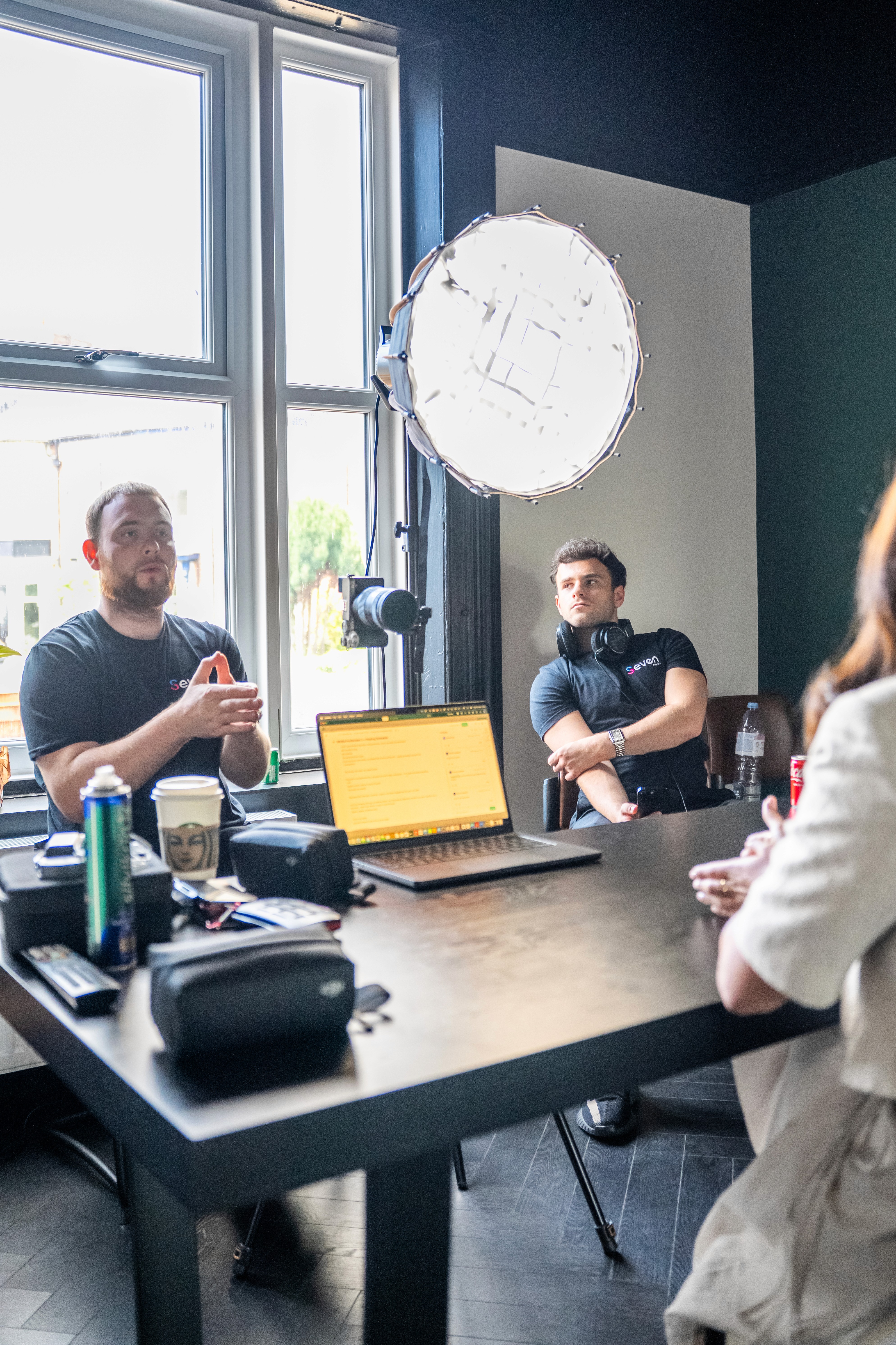 Dawid and Ronnie from the Seven Media team sit at a table planning the filming and content strategy for the day, with lighting equipment and a laptop open during the production meeting.