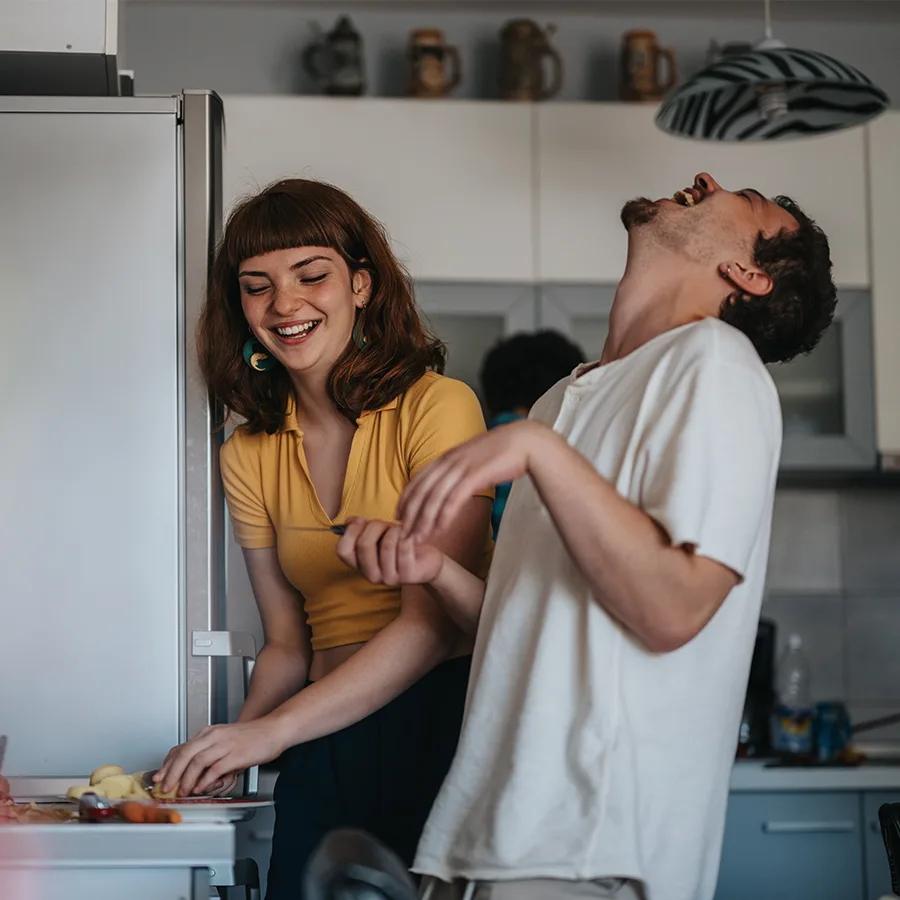 A young couple laughing together while preparing food in their kitchen