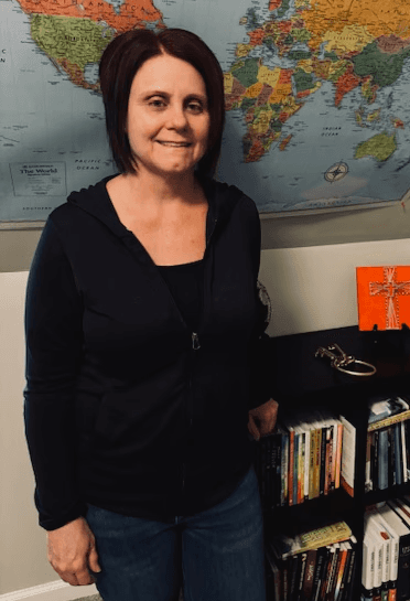 A young person with long, wavy hair sits in front of a plain background, looking directly at the camera.