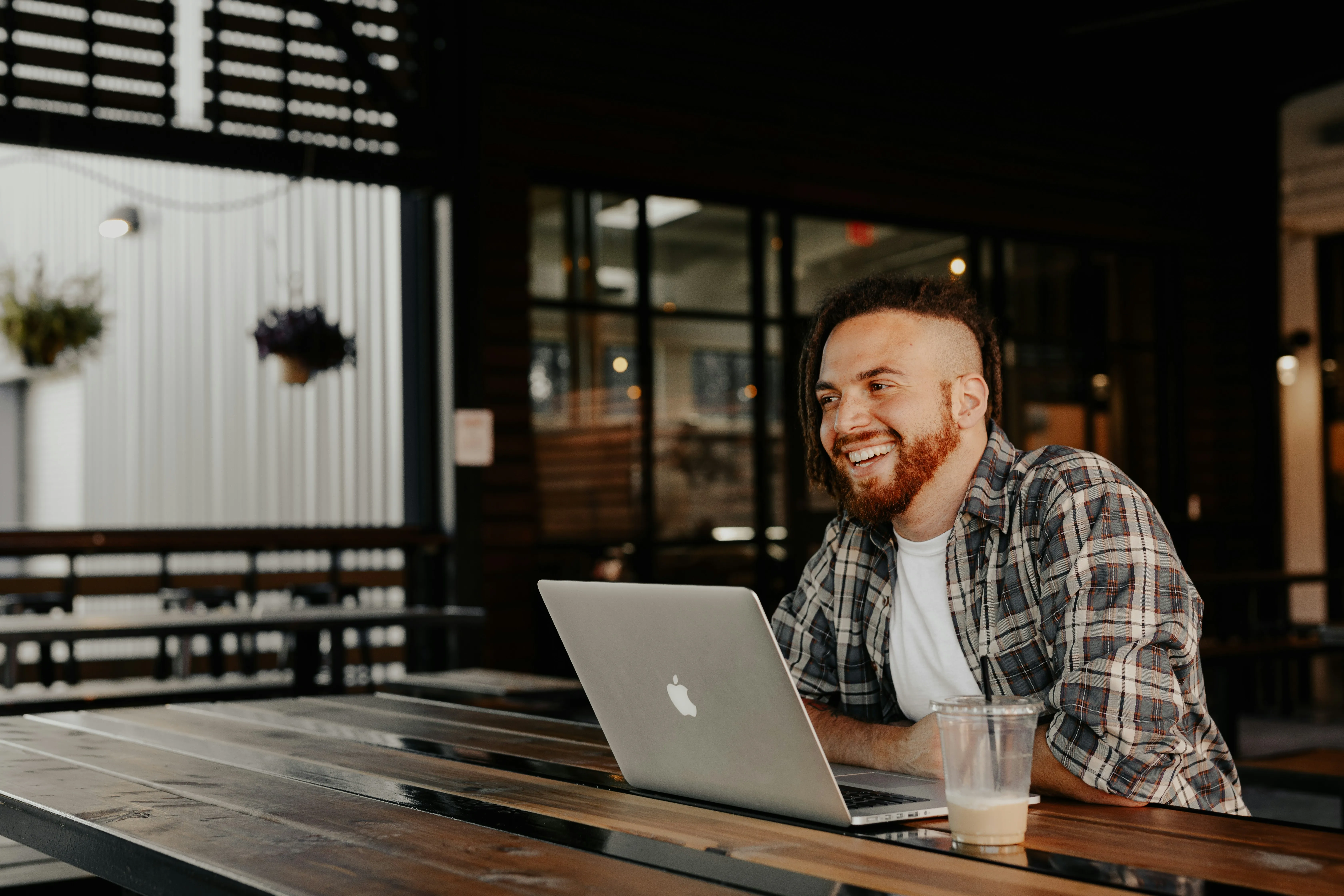 man in black and white plaid dress shirt sitting by the table using macbook