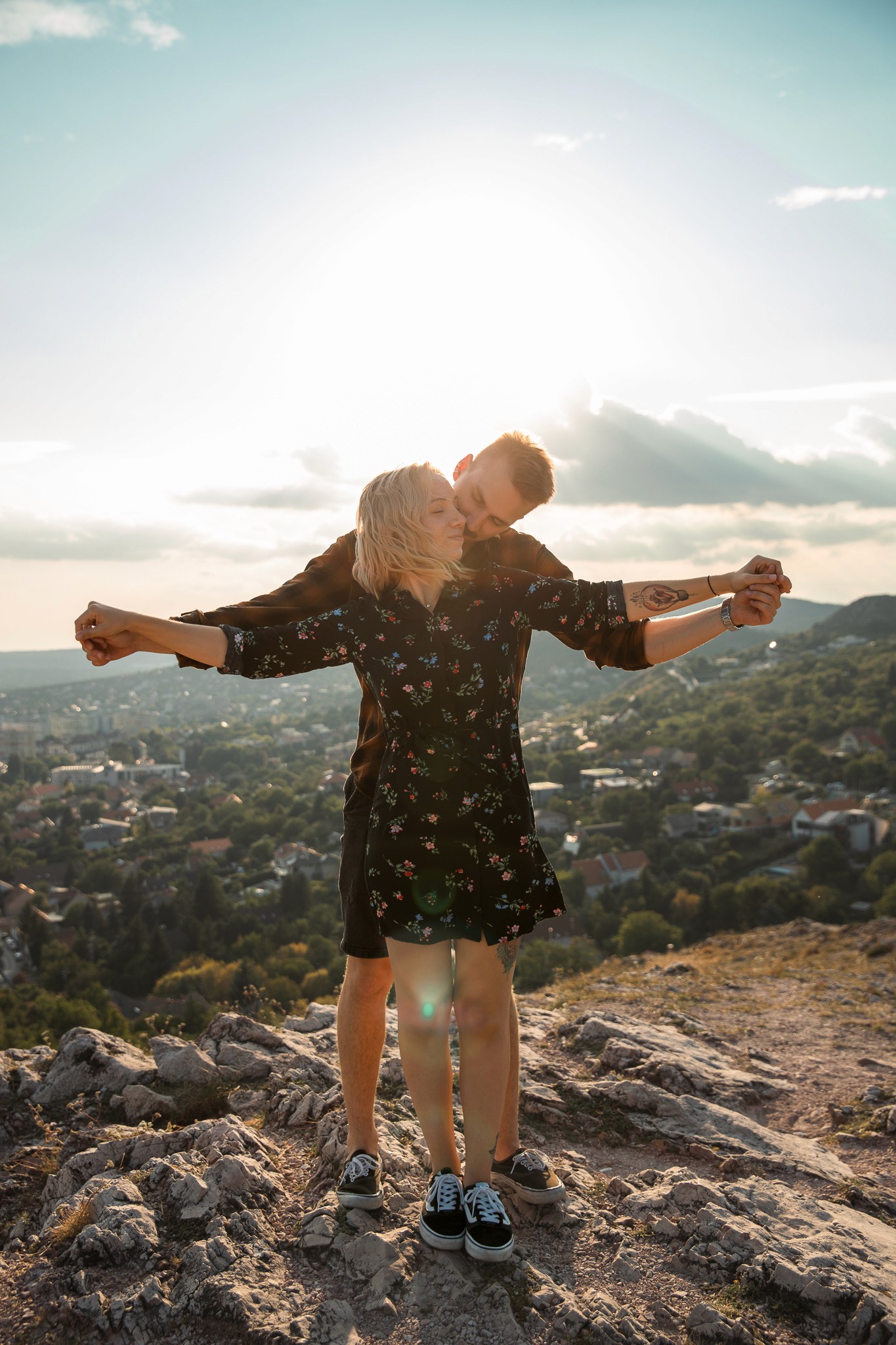 Fiatal pár naplementében ölelkezik egy hegytetőn.