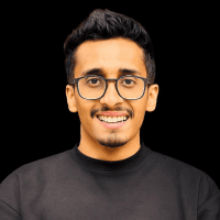 A smiling person with glasses, wearing a black shirt, poses against a dark background.