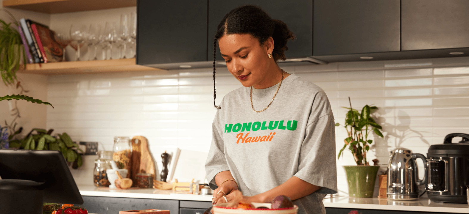 Woman in a home kitchen chops vegetables while wearing a grey shirt