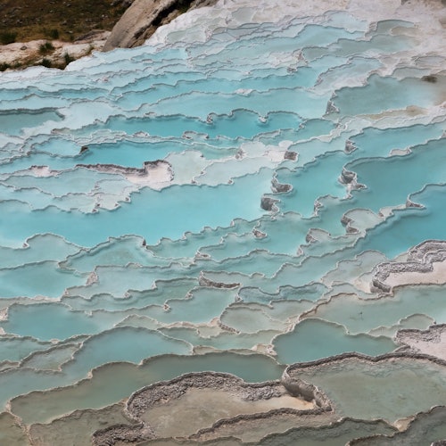 Mababaw na mga mala-turkesa na kaskas na mga pool na may puting gilid na puno ng mineral, na kahawig ng isang natural, hagdan-hagdang anyo.