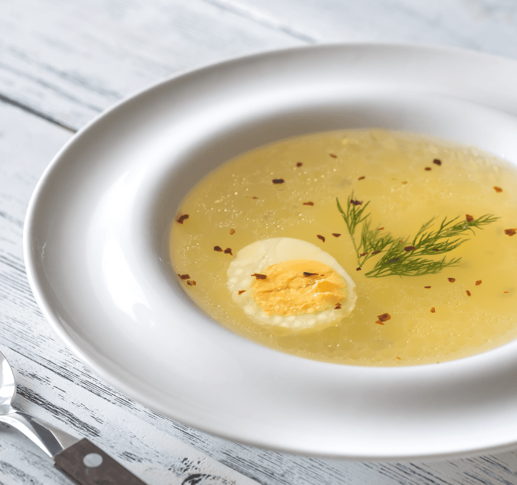 Clear golden broth with a perfectly halved hard-boiled egg, garnished with fresh dill and red pepper flakes, showcasing.