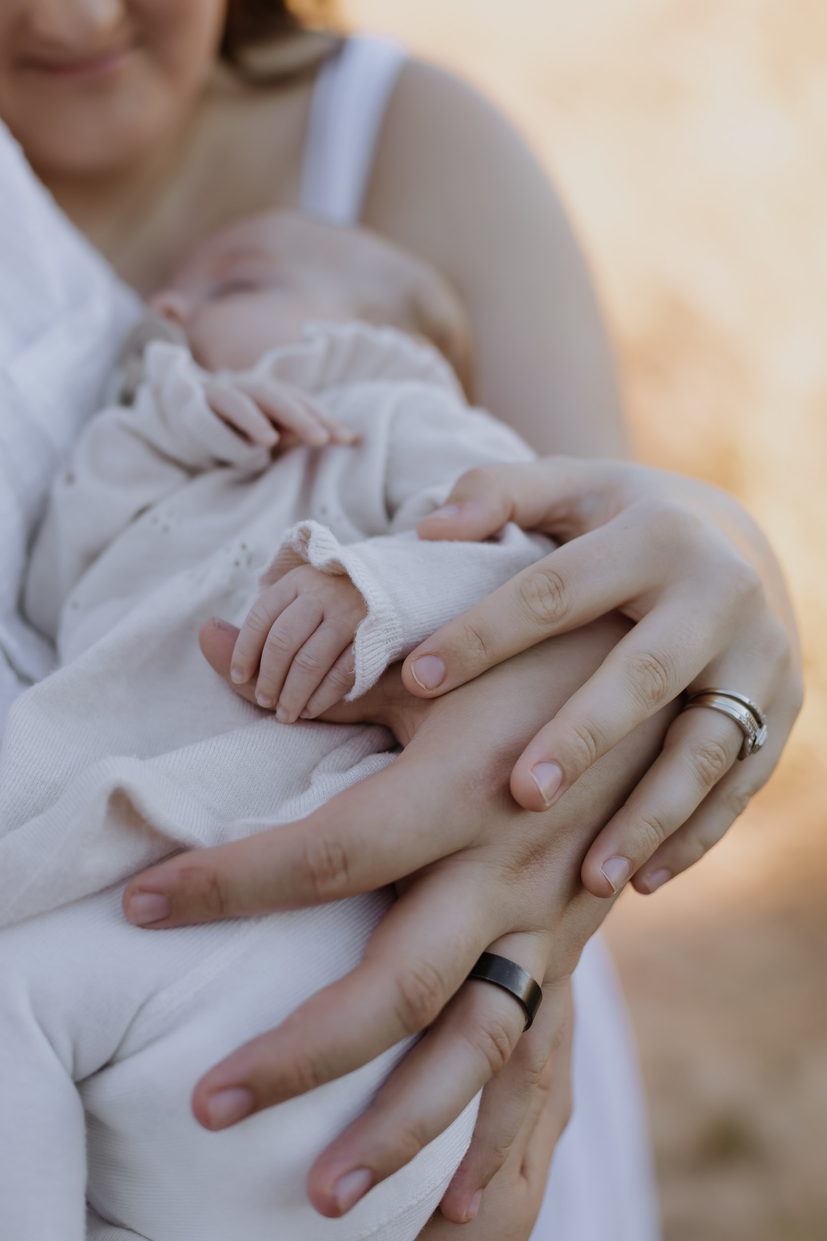 Close up of parents hands holding newborn baby's hand with glowing sunset in Mackay