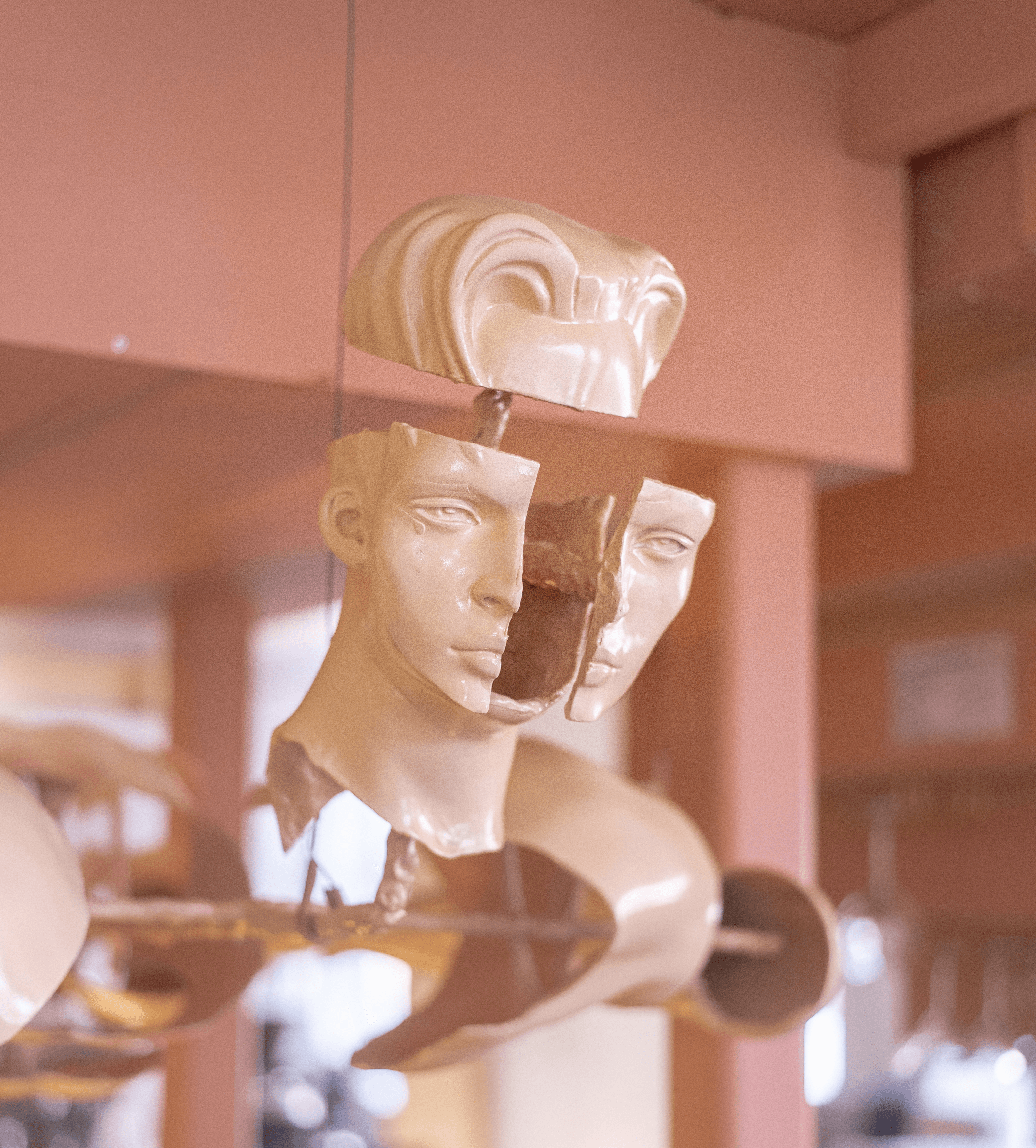 Sculptures of human heads and figures suspended in an indoor space with warm lighting and wooden accents.