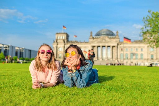 Two women sitting on grass smiling in front of a historic palace.