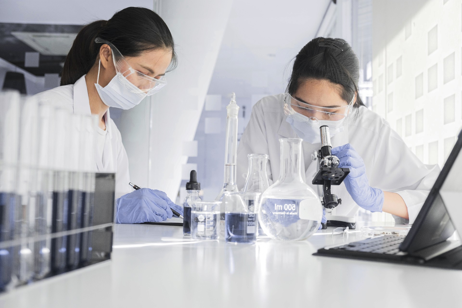Two scientists in a lab on a research enviorment, wearing masks, goggles, and gloves.