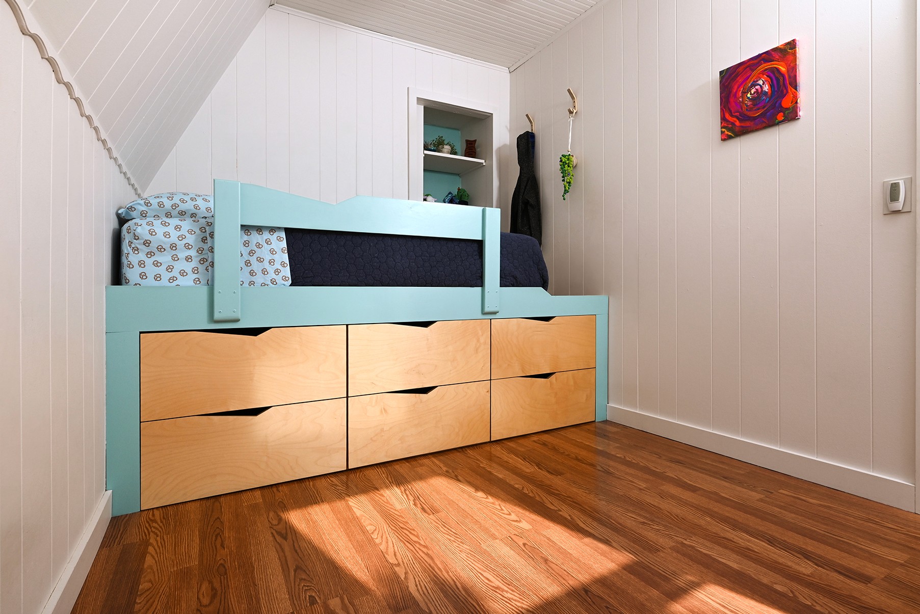 Kids room with tall blue bed with wooden drawers