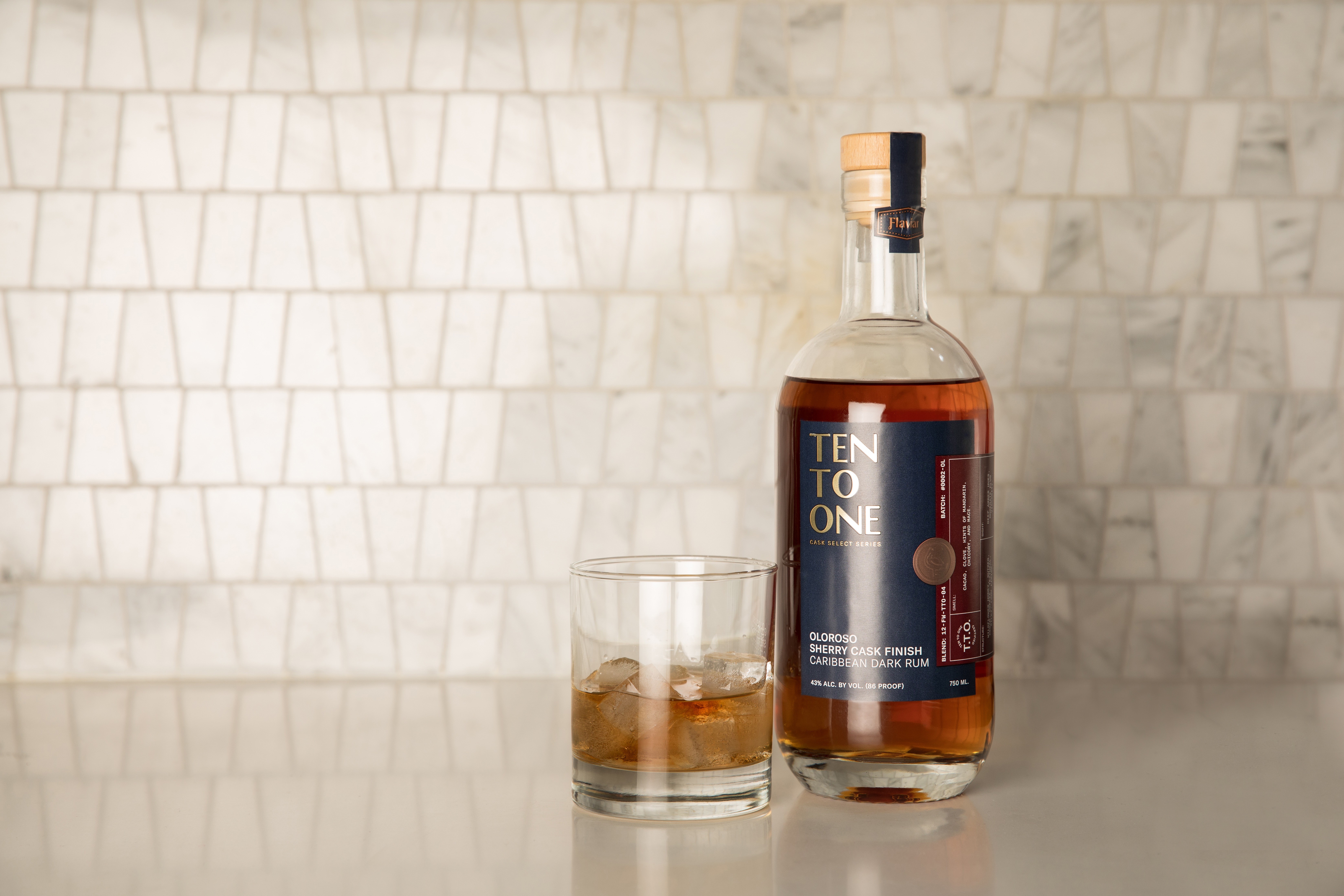 Ten To One rum bottle beside a rocks glass with ice on a light countertop.
