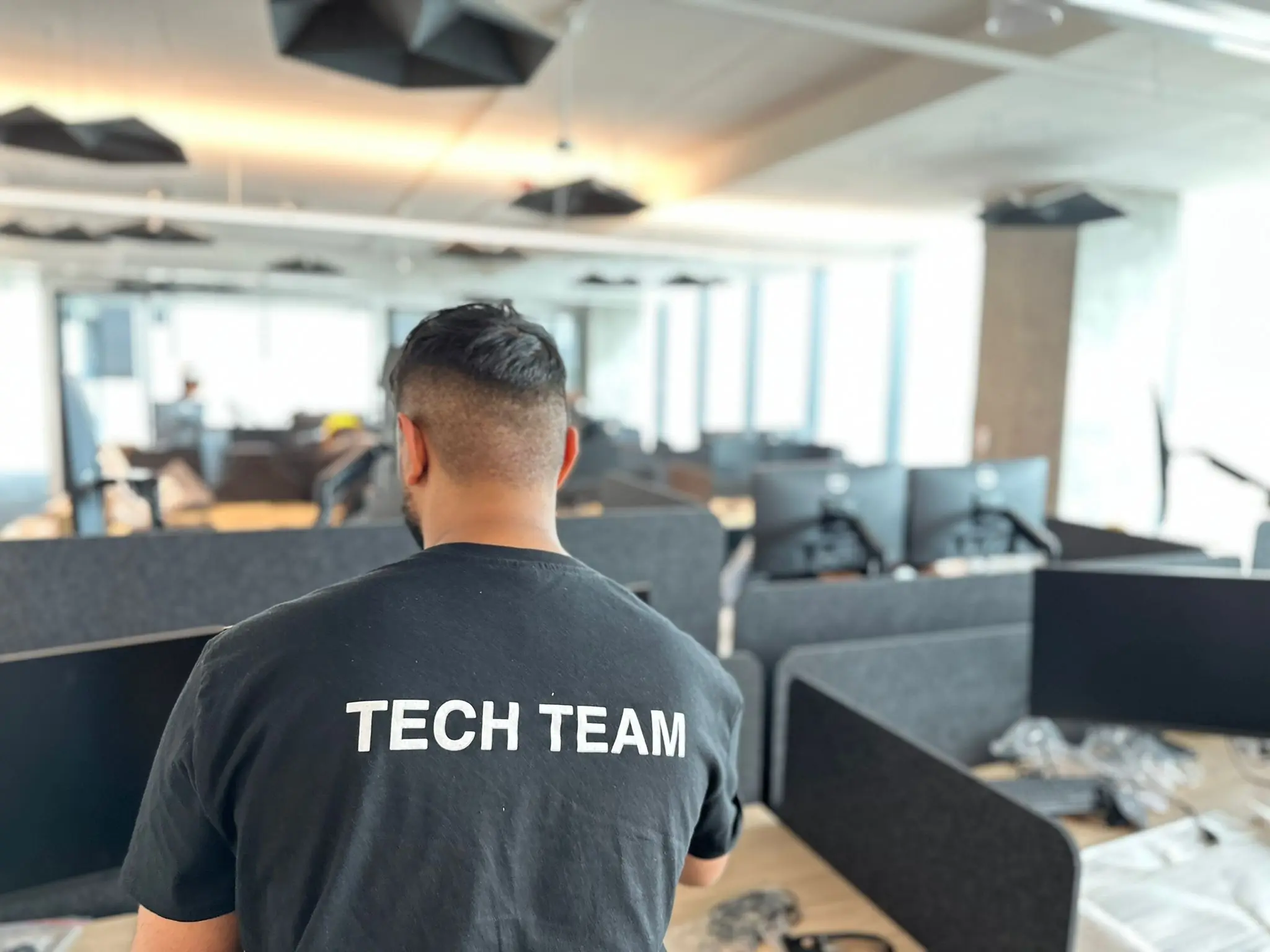 IT support team member working in a modern office environment with workstations and business setup in the background