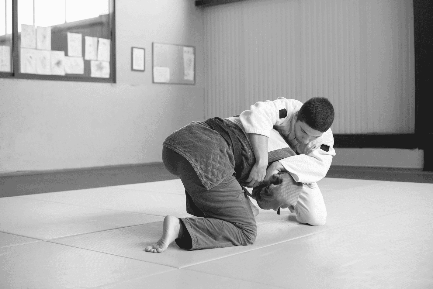 A young martial arts student in a blue gi working for a grip and breakdown on a training partner wearing a white gi on yellow mats.