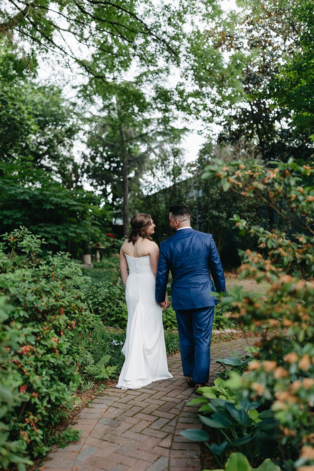 Bride walking through a garden gate with the groom following behind her.