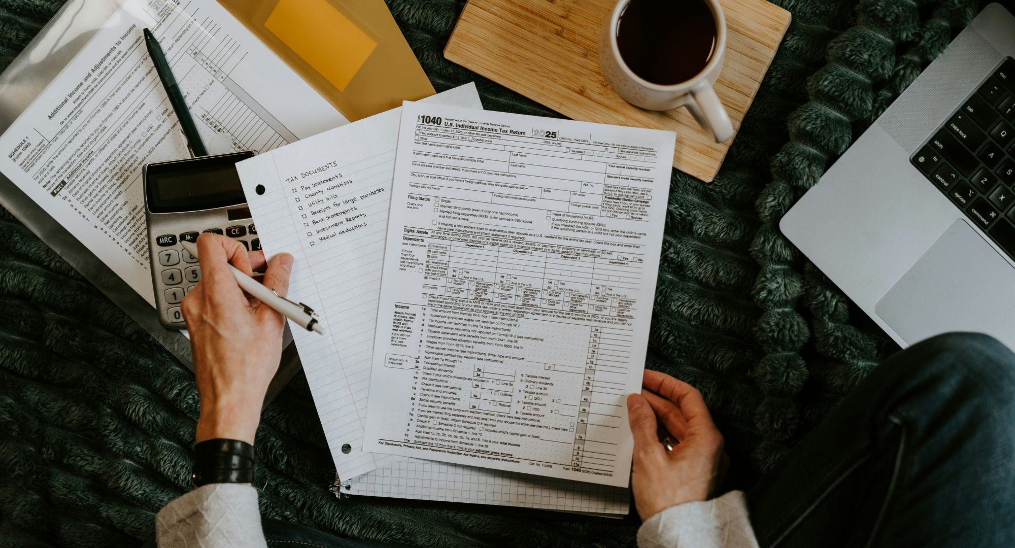 Pessoa revisando documentos de tributos, com calculadora e notebook