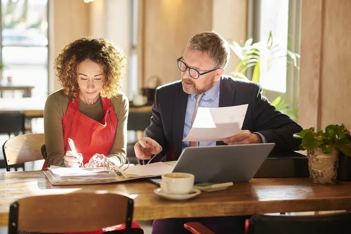 Financial consultant and small business owner discussing documents at a table.