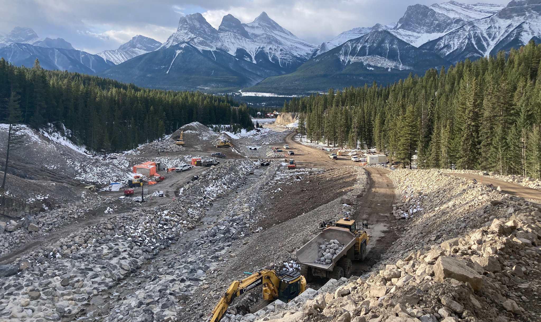 Steep construction access road and lock block retaining wall under construction at Cougar Creek Dam site near Canmore