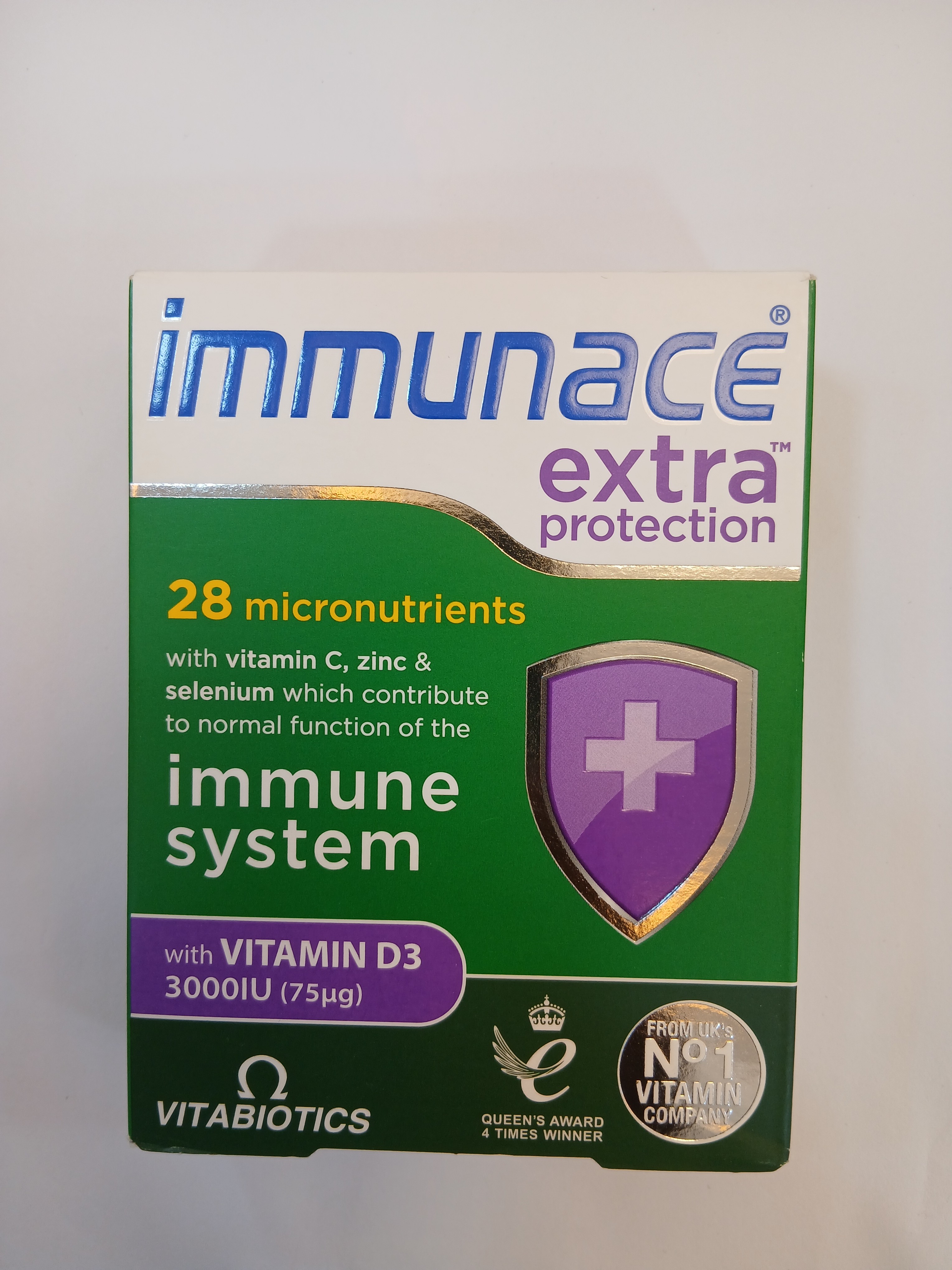 A white cardboard box with green and purple accents displays text about containing 28 micronutrients, including vitamin D3, zinc, selenium, and a shield graphic with a cross.