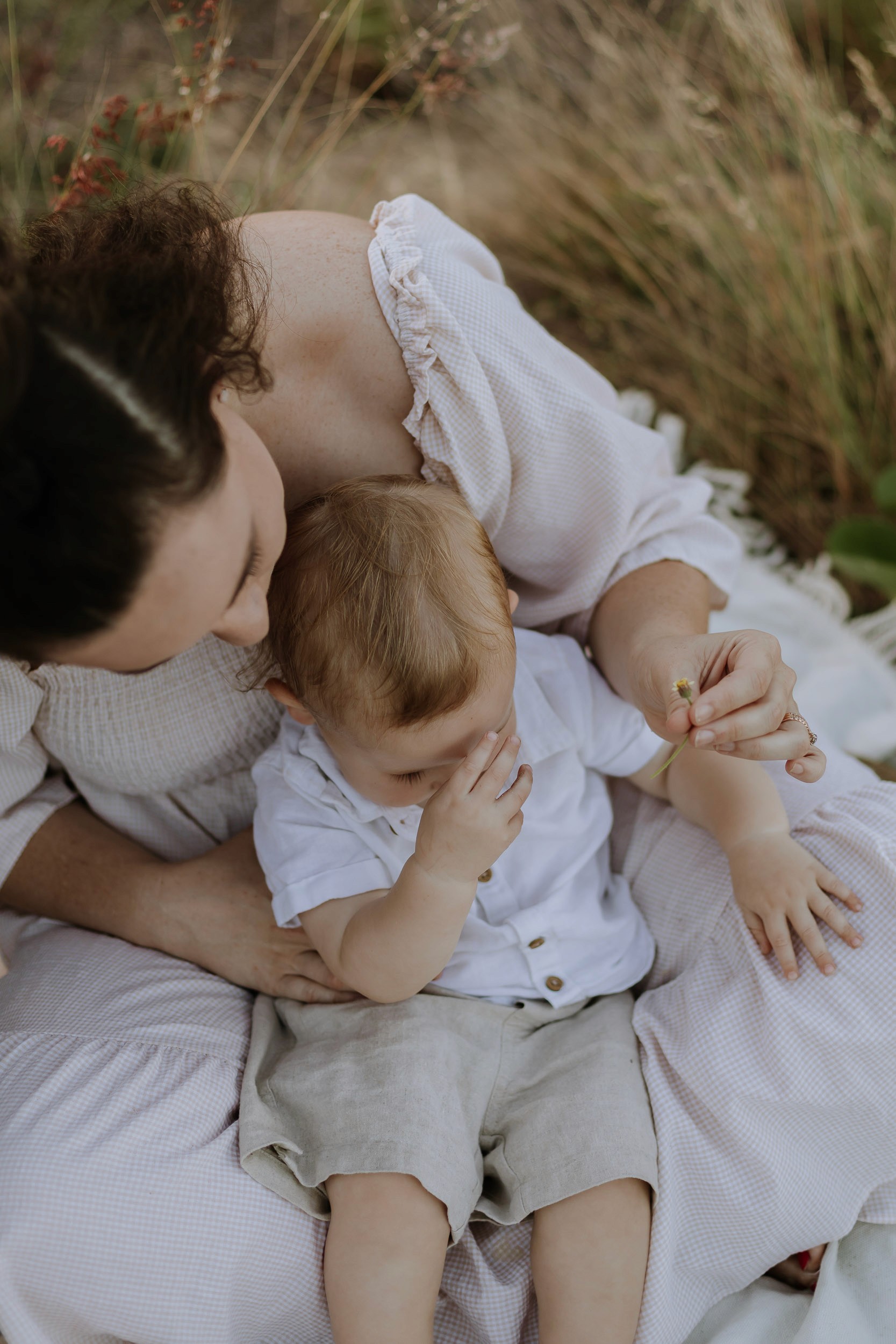 Arial view of mother sitting with child in the grass picking flowers during family photoshoot in Mackay