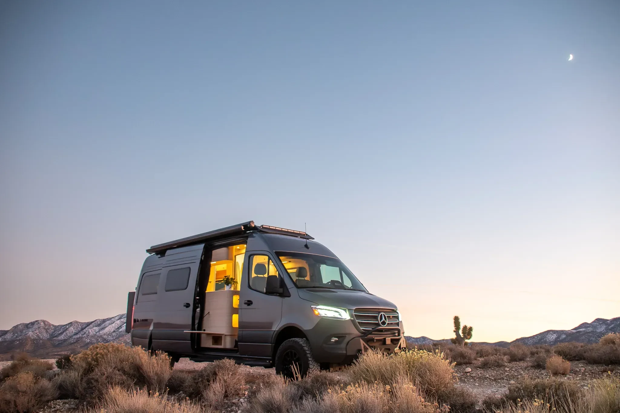 Camper van parked in the desert at dusk, interior lights glowing