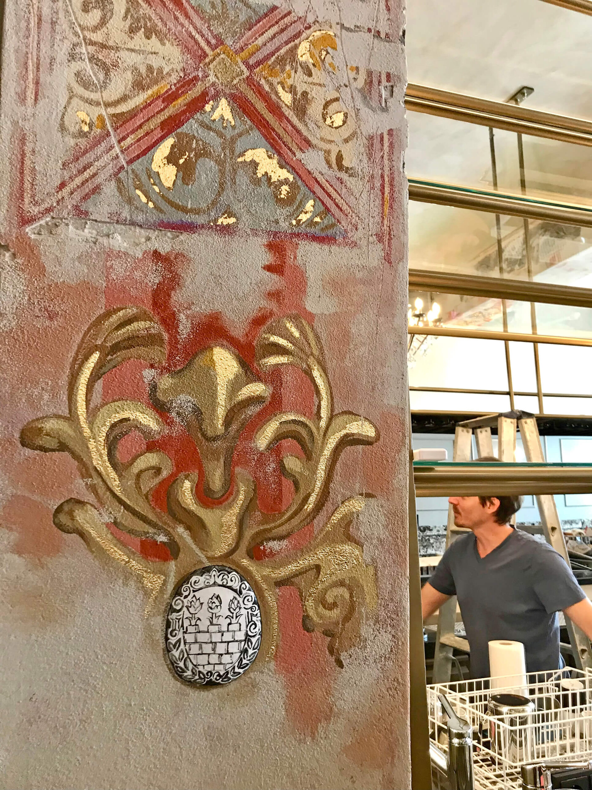 Nahaufnahme eines goldenen Zierornaments mit Emaille-Intarsie auf einer rot und grau gestalteten Wand.