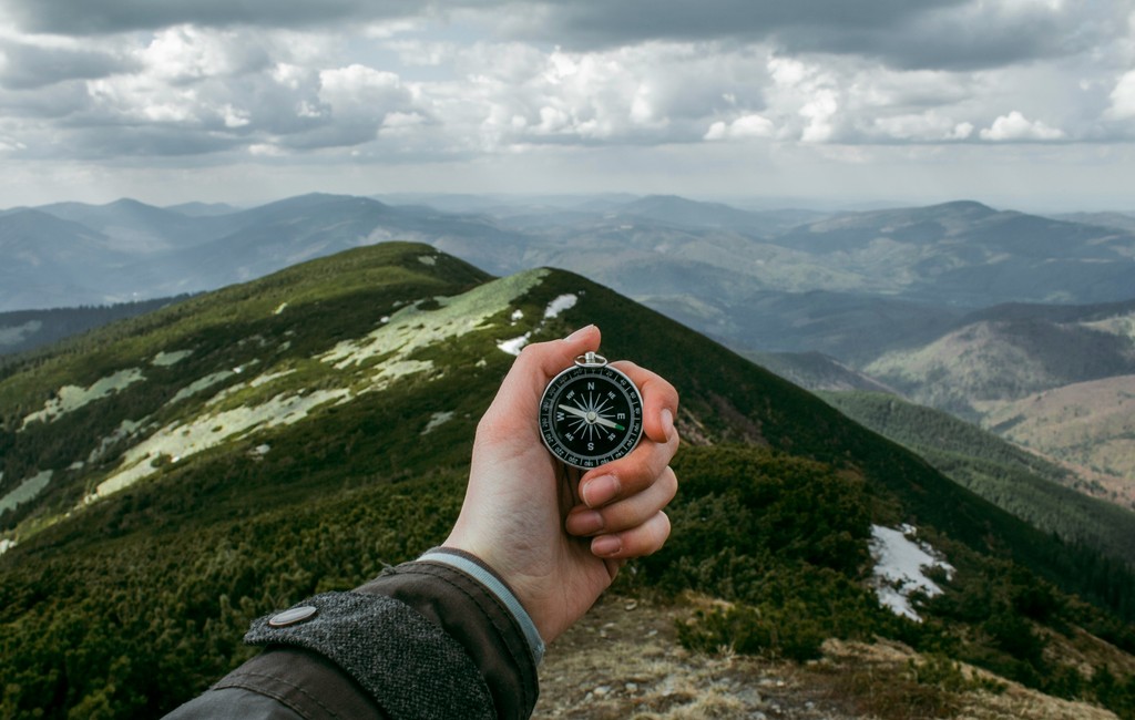 Hand holding compass on top of mountain signifying guidence and growth