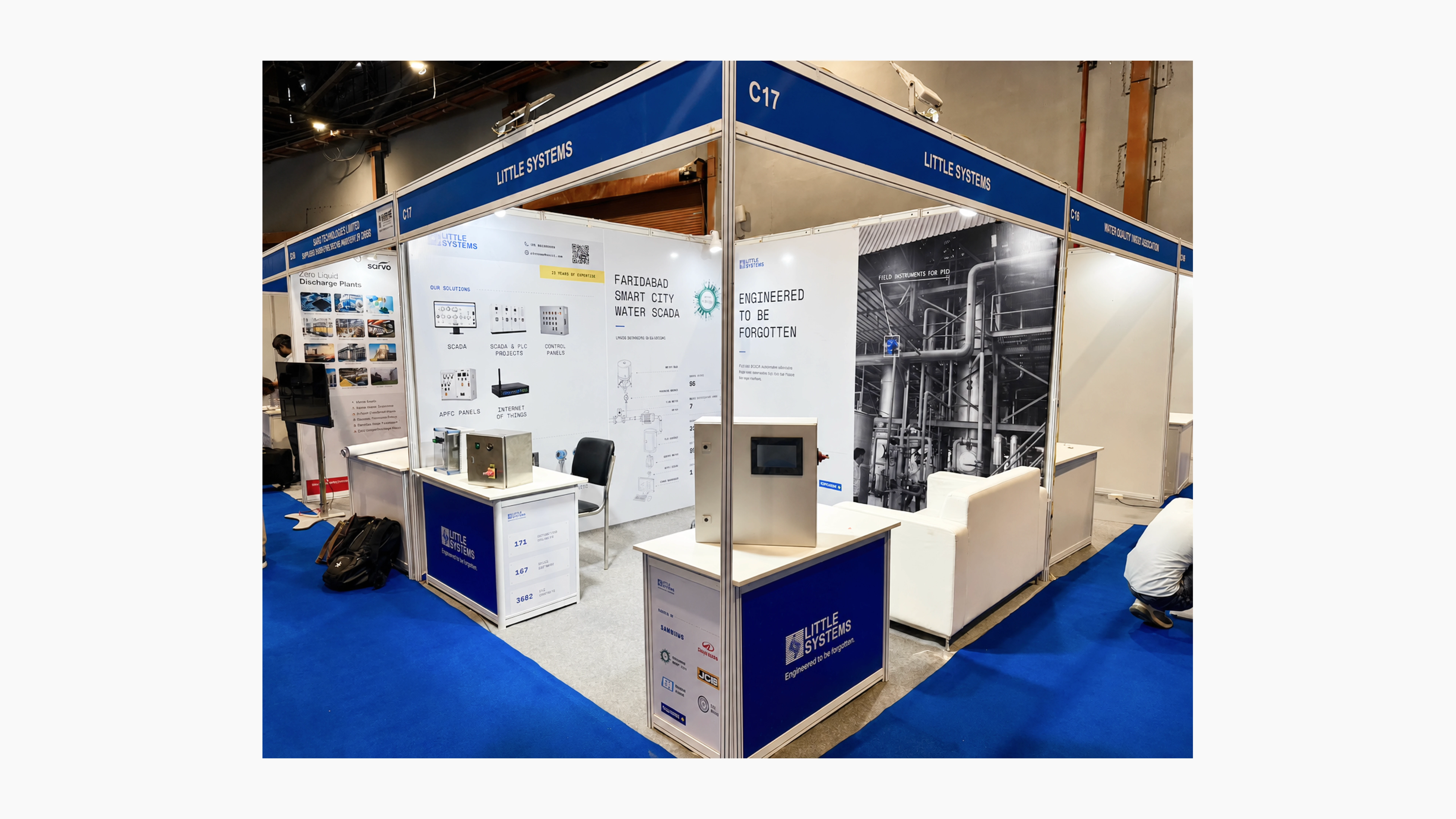 Front view of the Little Systems exhibition booth with blue overhead branding, technical solution displays, industrial equipment, control panels, and large wall graphics featuring industrial automation imagery.
