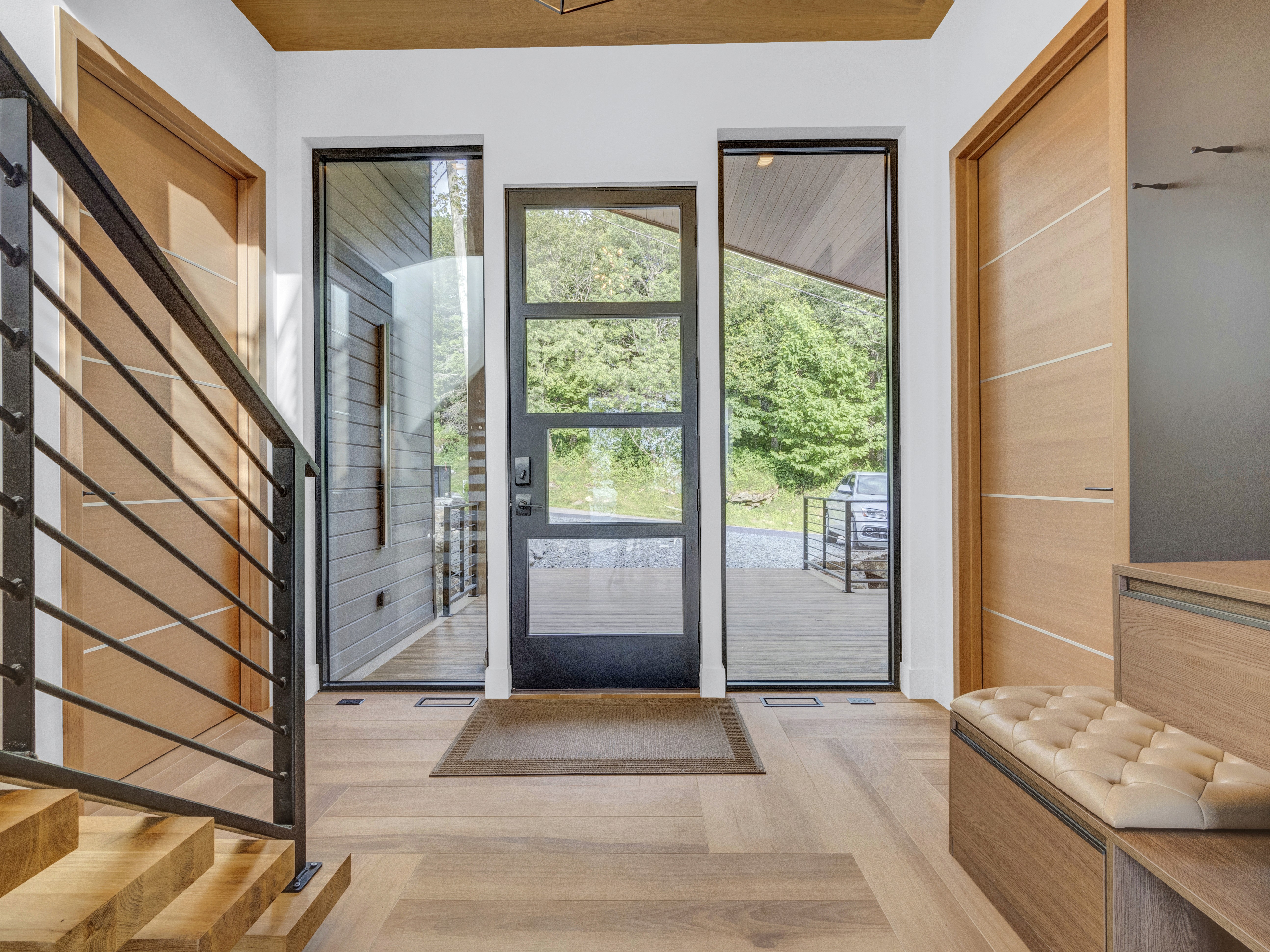 Interior view of the front entrance with floor-to-ceiling glass sidelights, a modern black door, and warm wood ceilings
