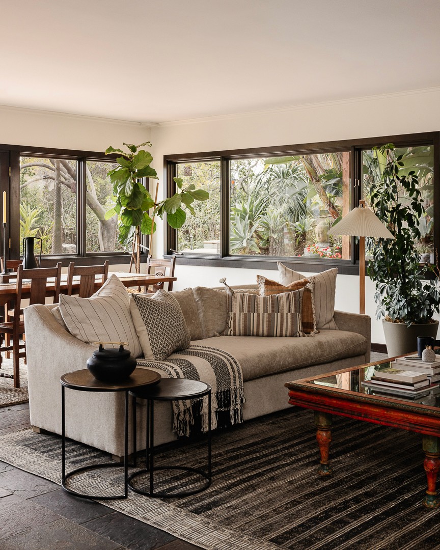 This outdoor living design blends modern luxury with nature, featuring a beach-club-style seating area, natural wood tones, lush greenery, and elegant pool stone accents for a tranquil retreat