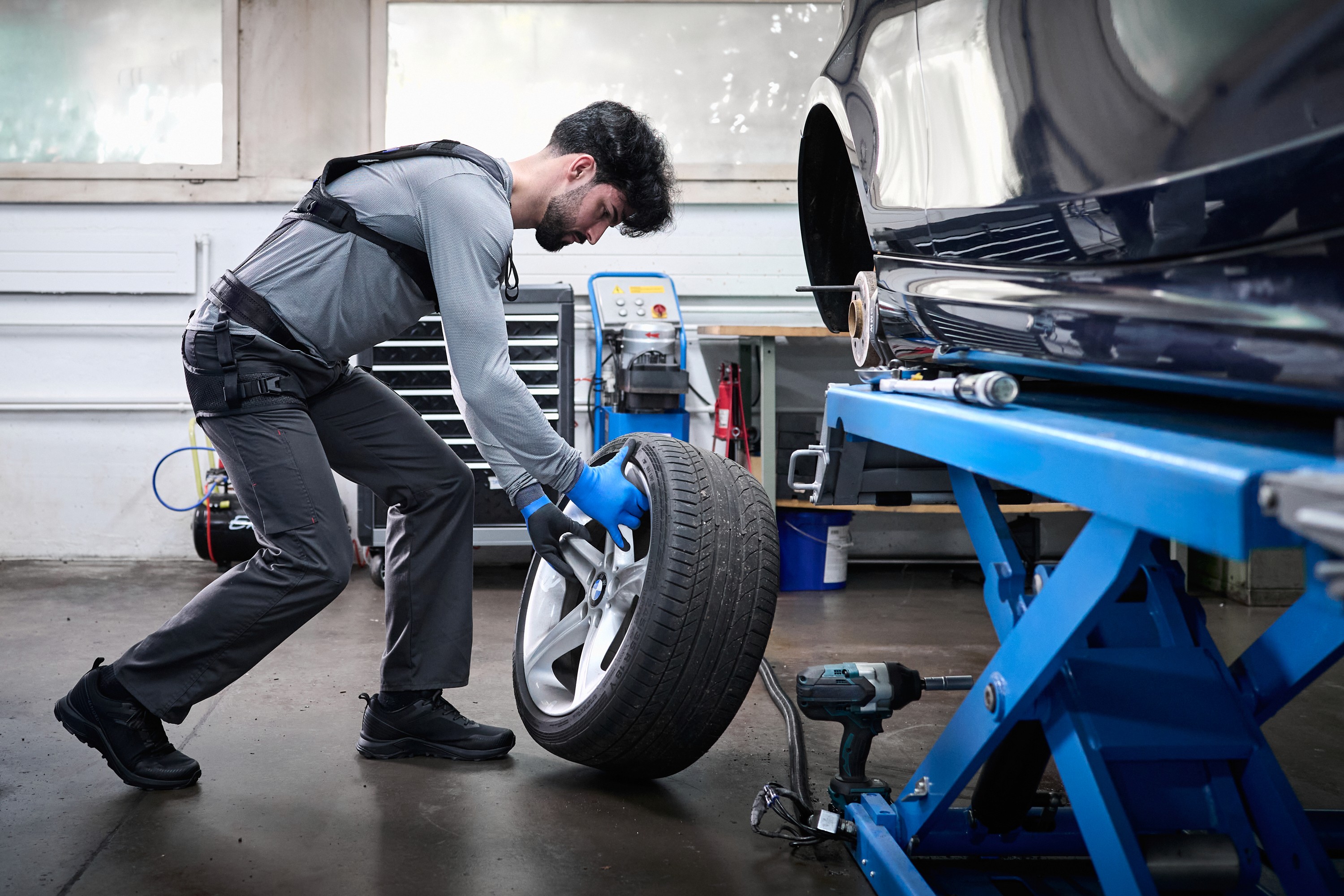 Mechanic wearing a Liftsuit exoskeleton in a garage in Quebec to lift a tire and reduce lower back fatigue.
