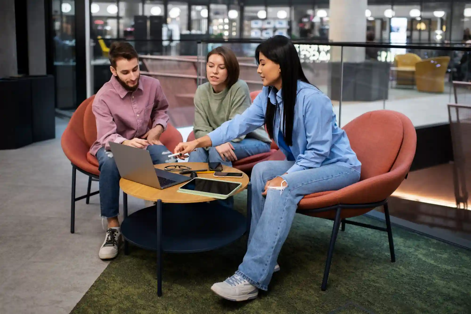 Diverse colleagues collaborating on a project using a laptop in a modern, casual office lounge setting.